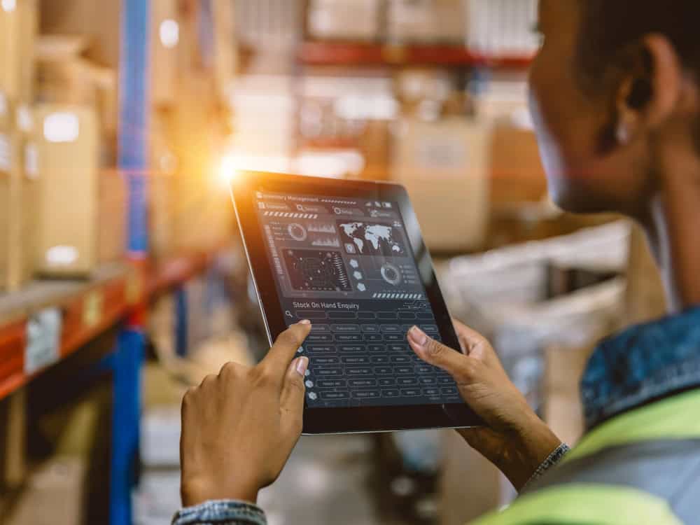 Warehouse worker using a tablet with an inventory management dashboard among storage shelves