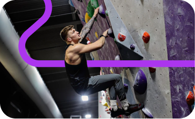 Man climbing an indoor bouldering wall with colorful holds under artificial lighting.