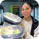 Smiling woman holding plastic containers with food inside in a bright indoor setting.