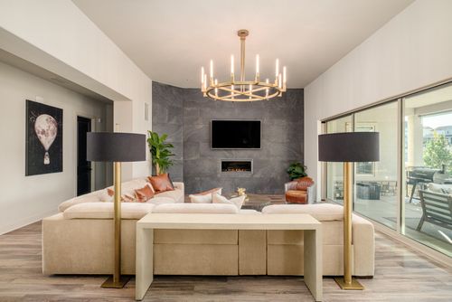 Modern living room with beige sectional sofa, two tall floor lamps with black shades, a gray stone fireplace wall with TV above, and large sliding glass doors.