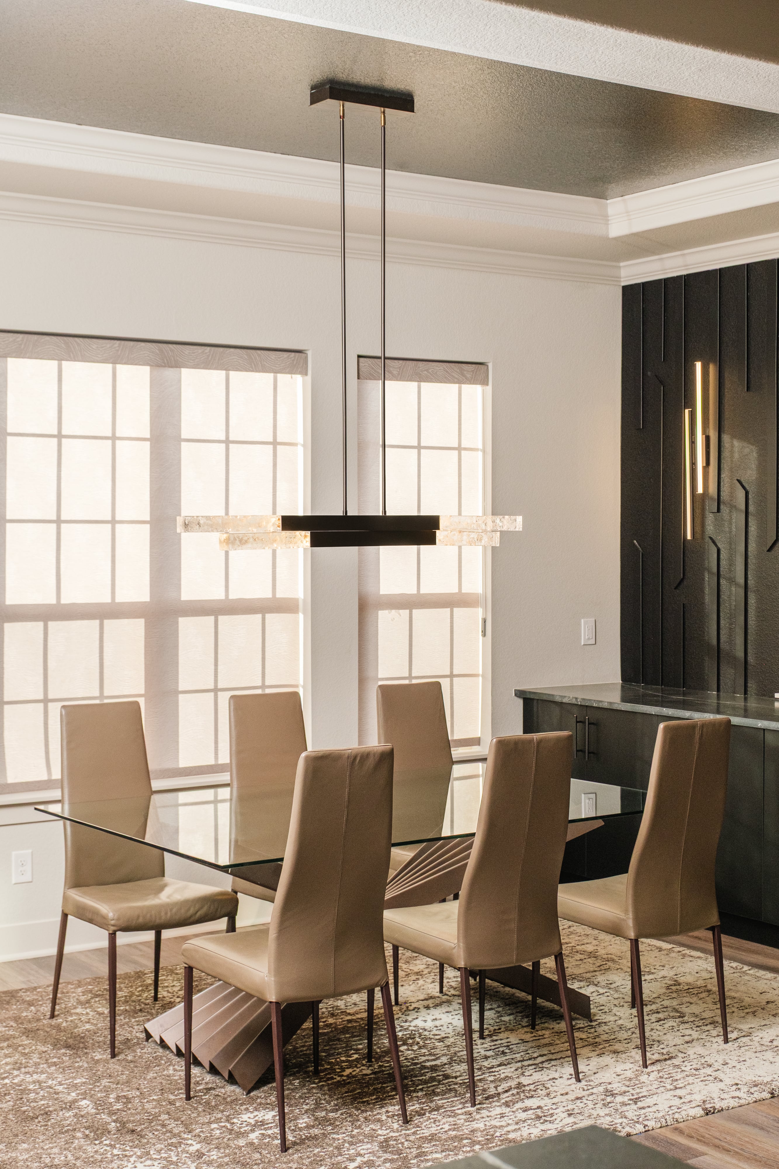 Modern dining room with a glass-top table, six brown leather chairs, a pendant light fixture, and large windows with sheer blinds.