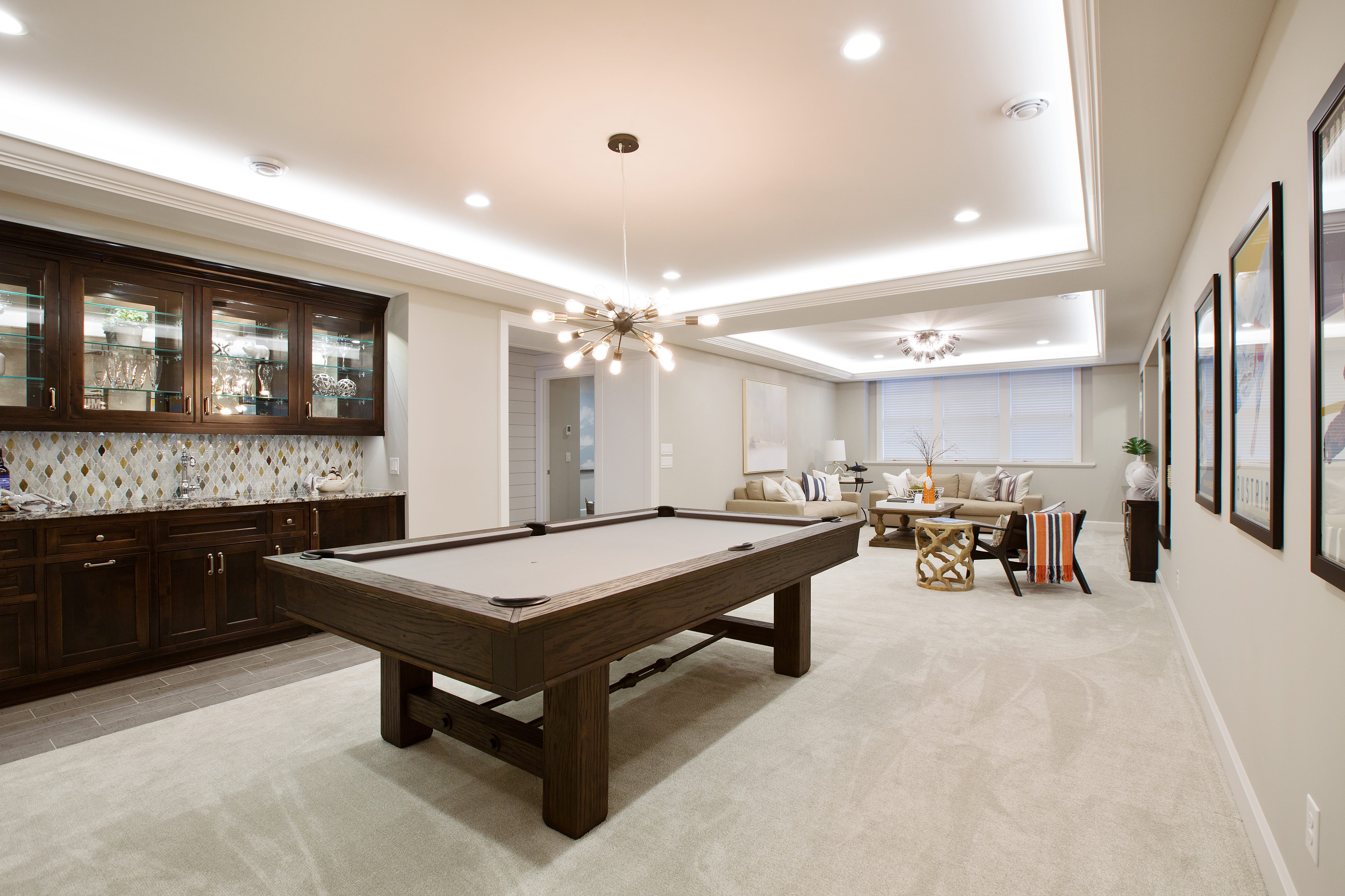 Modern basement game room with a pool table, dark wood cabinetry, a cozy seating area, and neutral-tone decor.