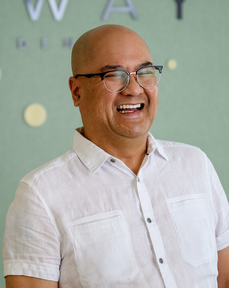 Smiling bald man wearing round glasses and a white short-sleeve shirt against a green background.