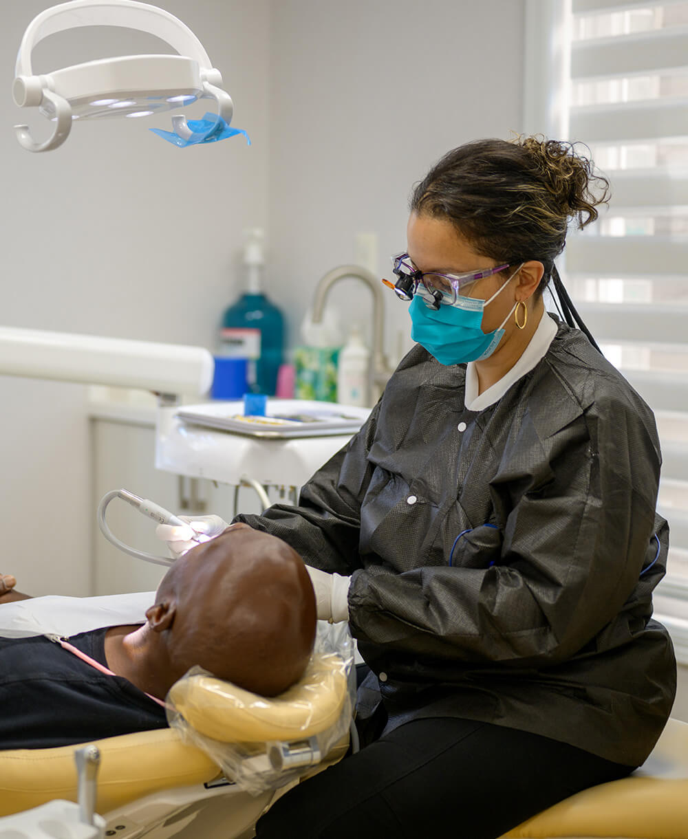 Dentist wearing magnifying glasses and a blue mask examines a patient reclining in a dental chair.