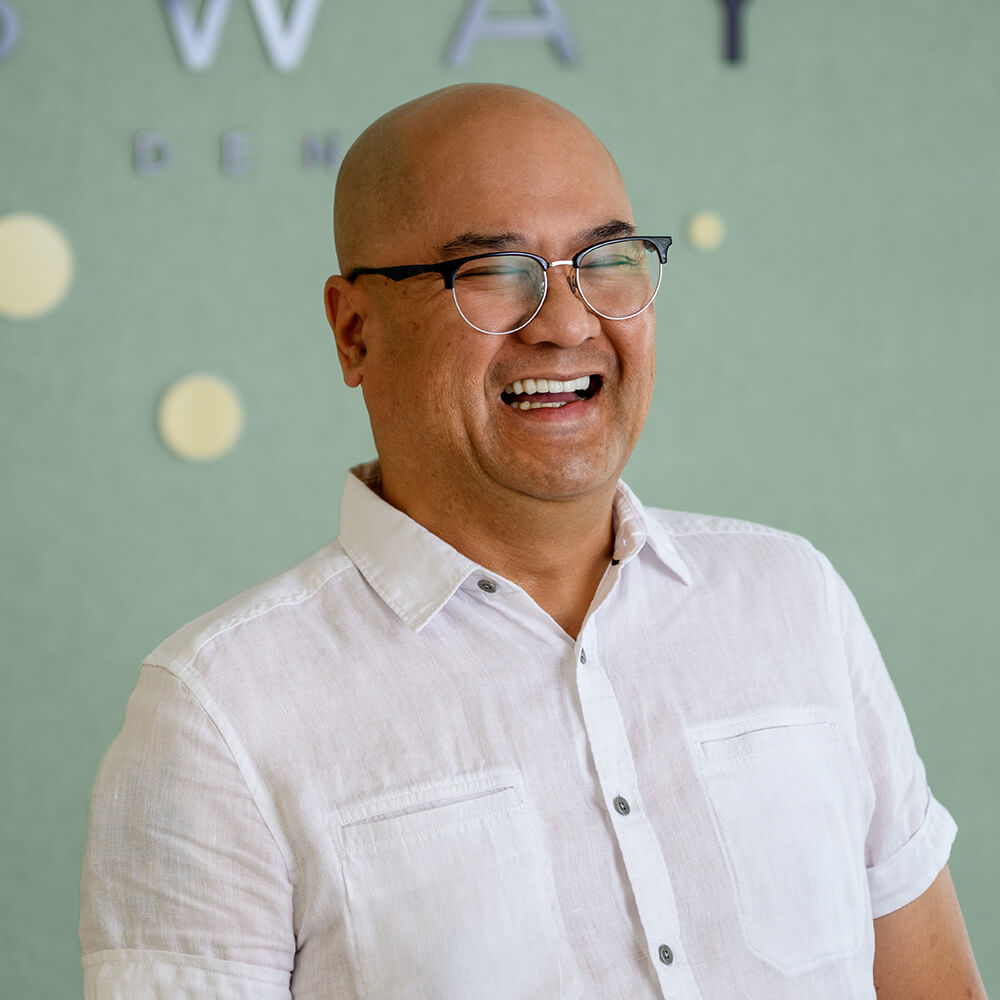 Smiling bald man with glasses wearing a white button-up shirt against a green background.