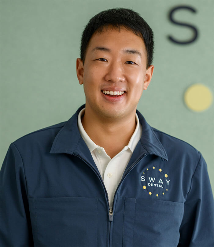 Smiling man wearing a navy jacket with SWAY Dental logo and a white collared shirt.