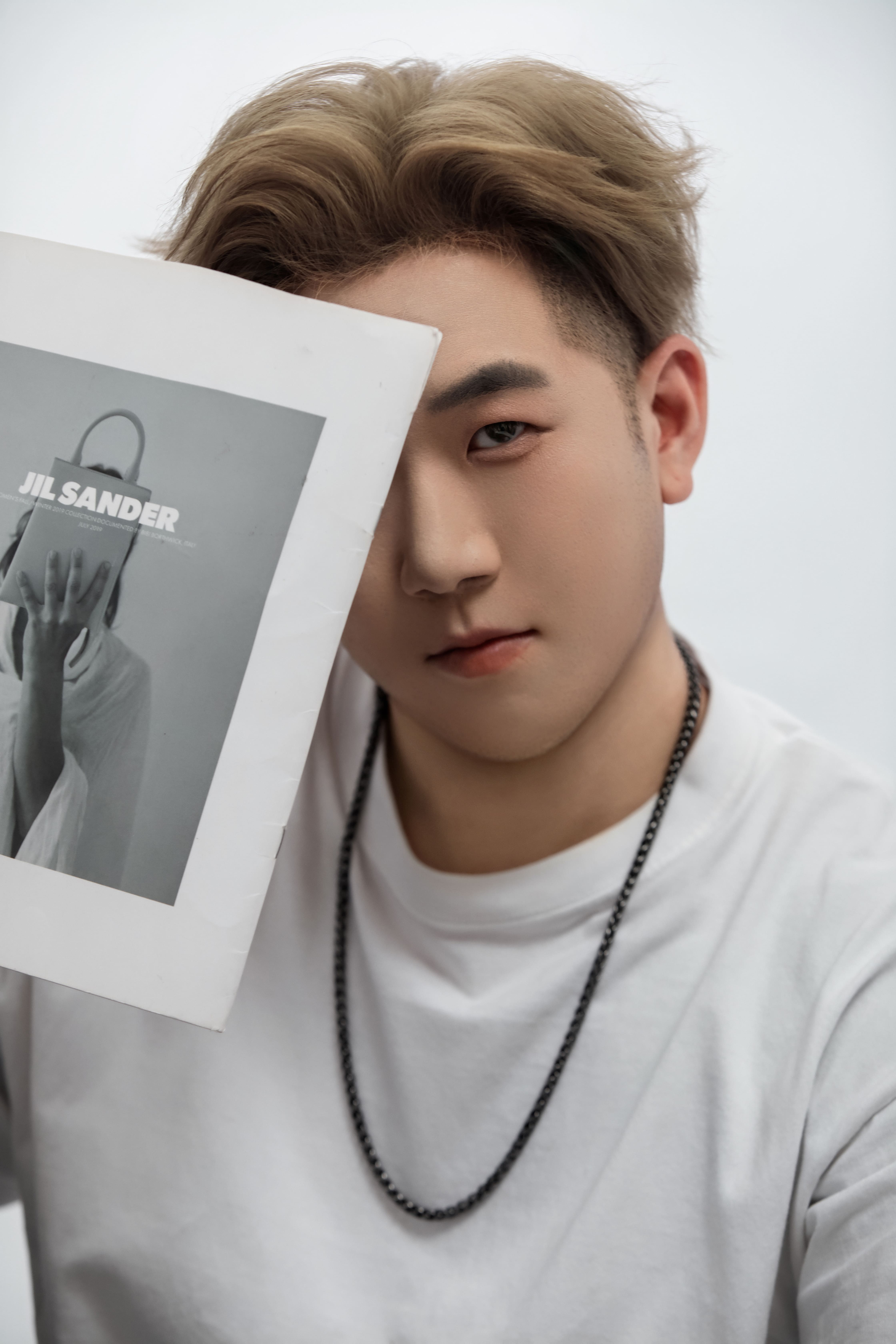 Using a Jil Sander poster to cover half his face, a man keeps one eye open.