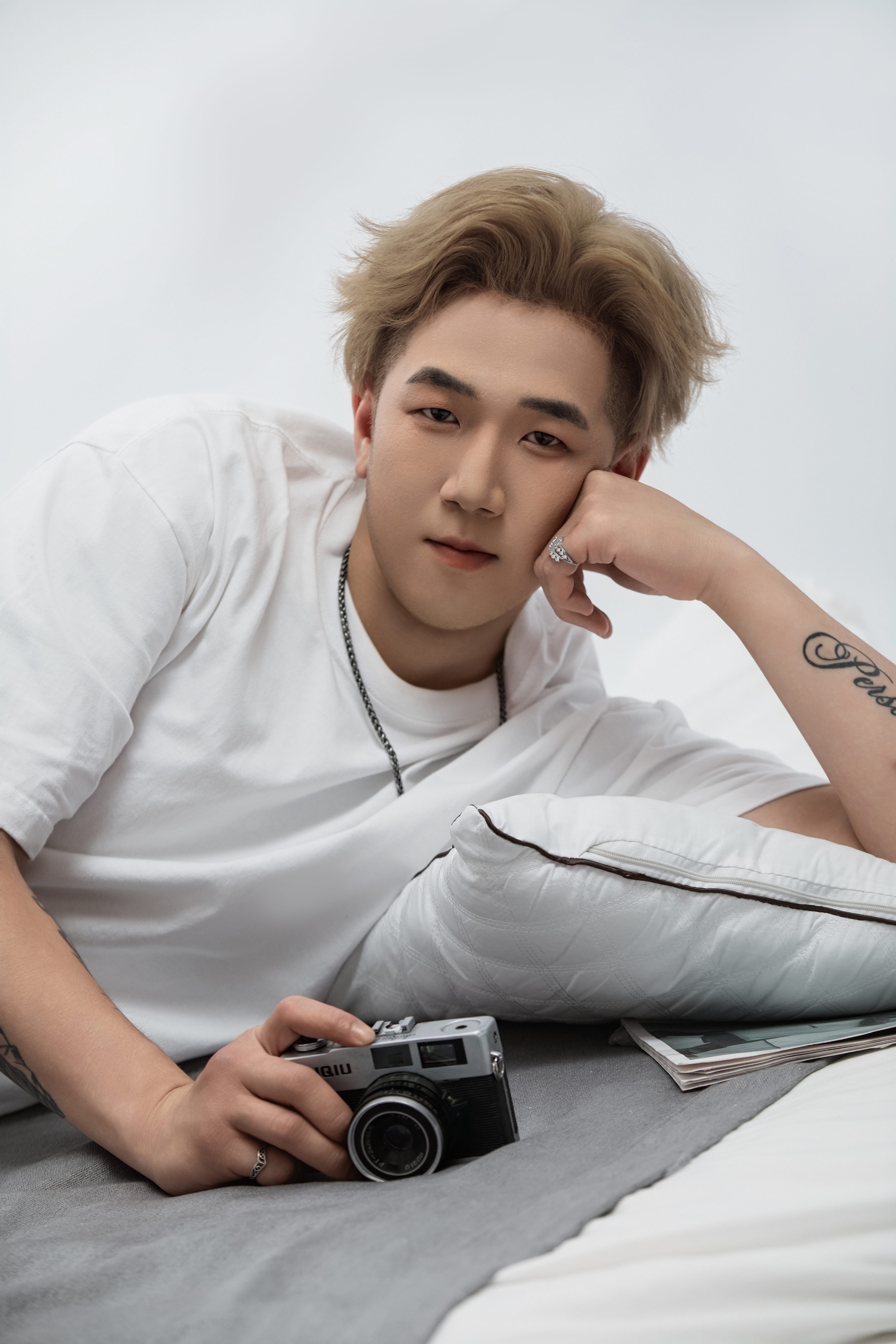 Lying on a rug, a man props his head with one hand and places the other on a camera before him.