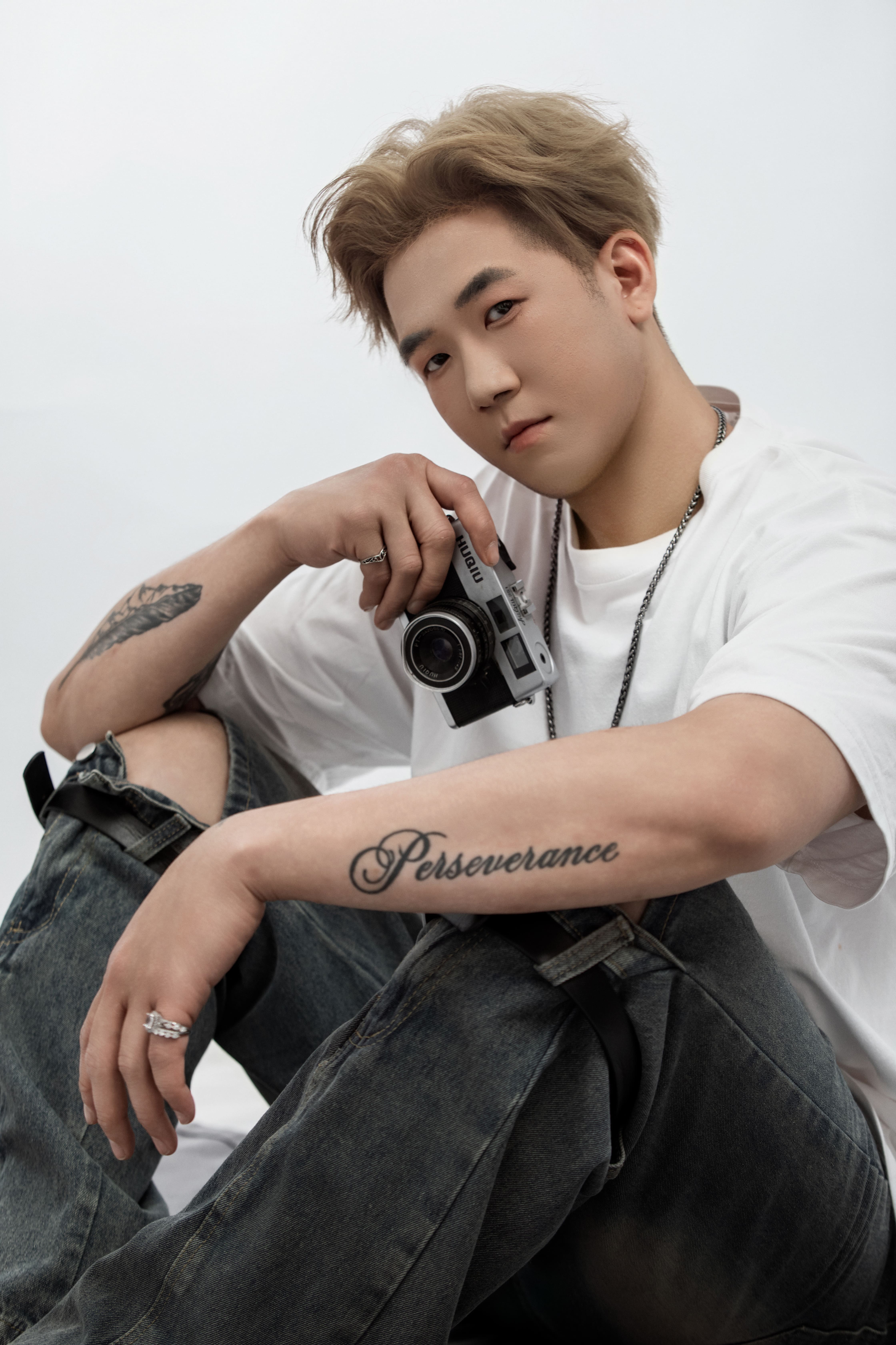 Seated on a rug, a man carefully holds a retro camera.