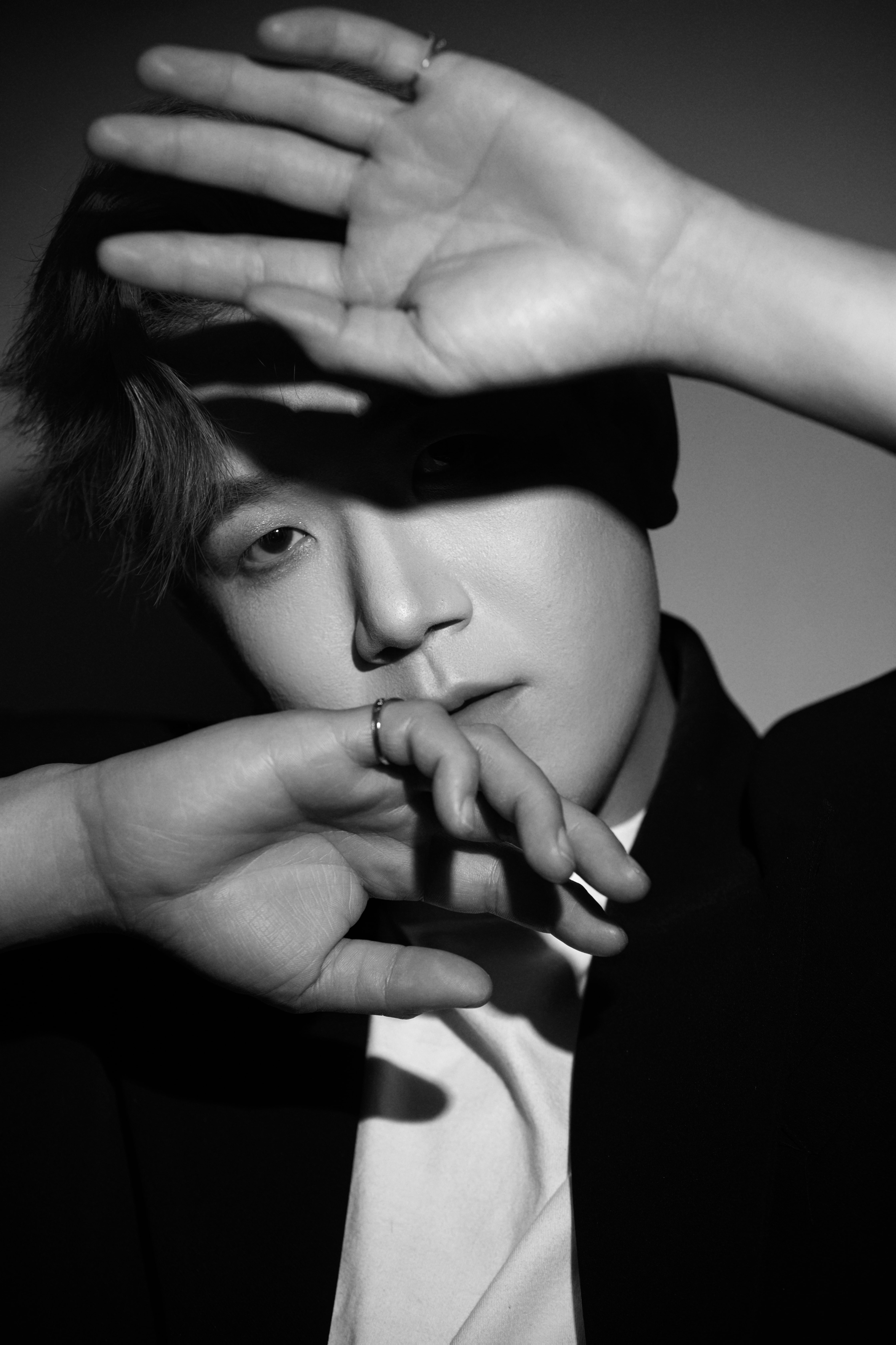 A man stands, shielding his face from the light with his hand.