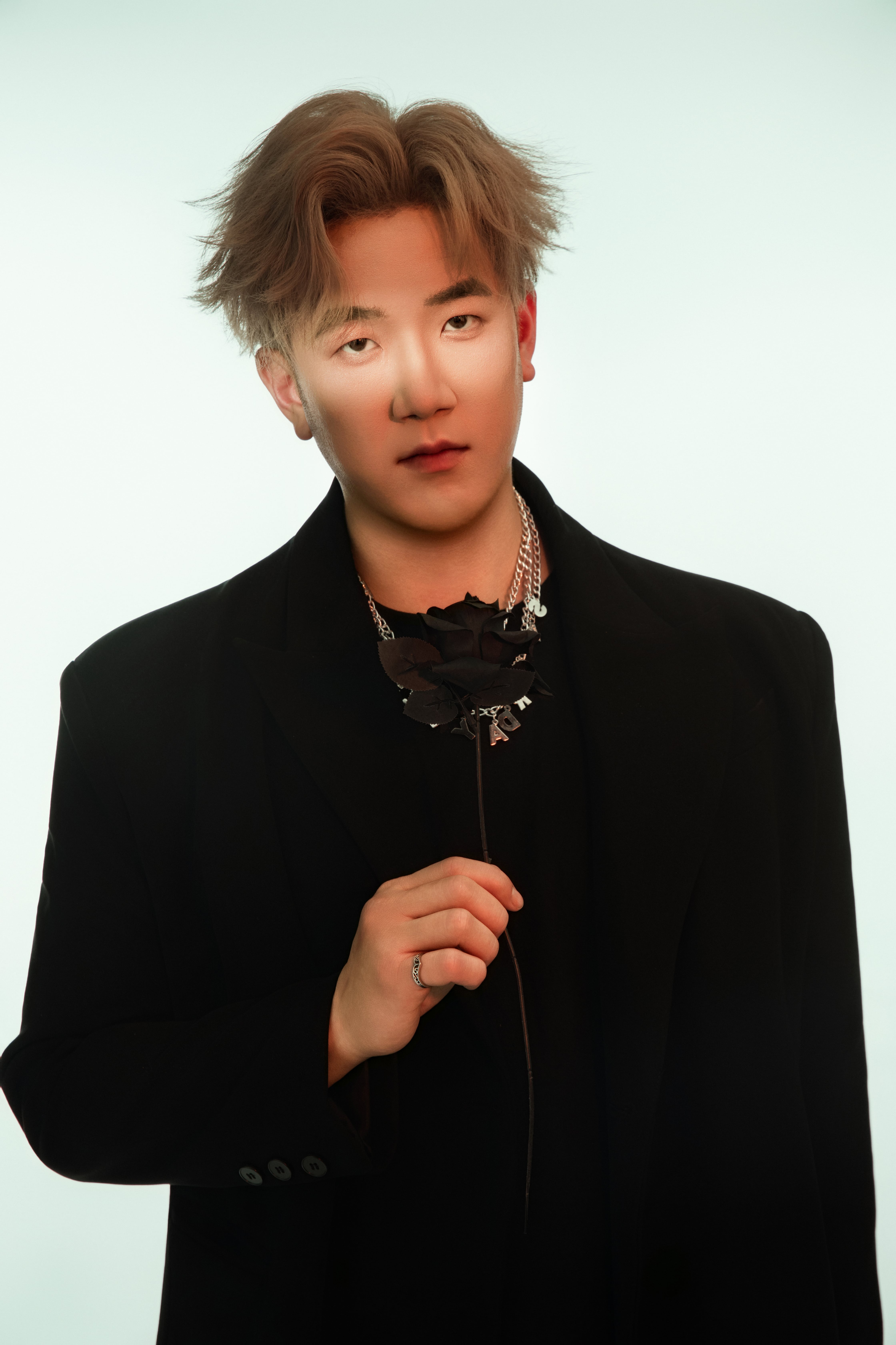 A man poses with a black rose in hand, emerald-green light washing the background.