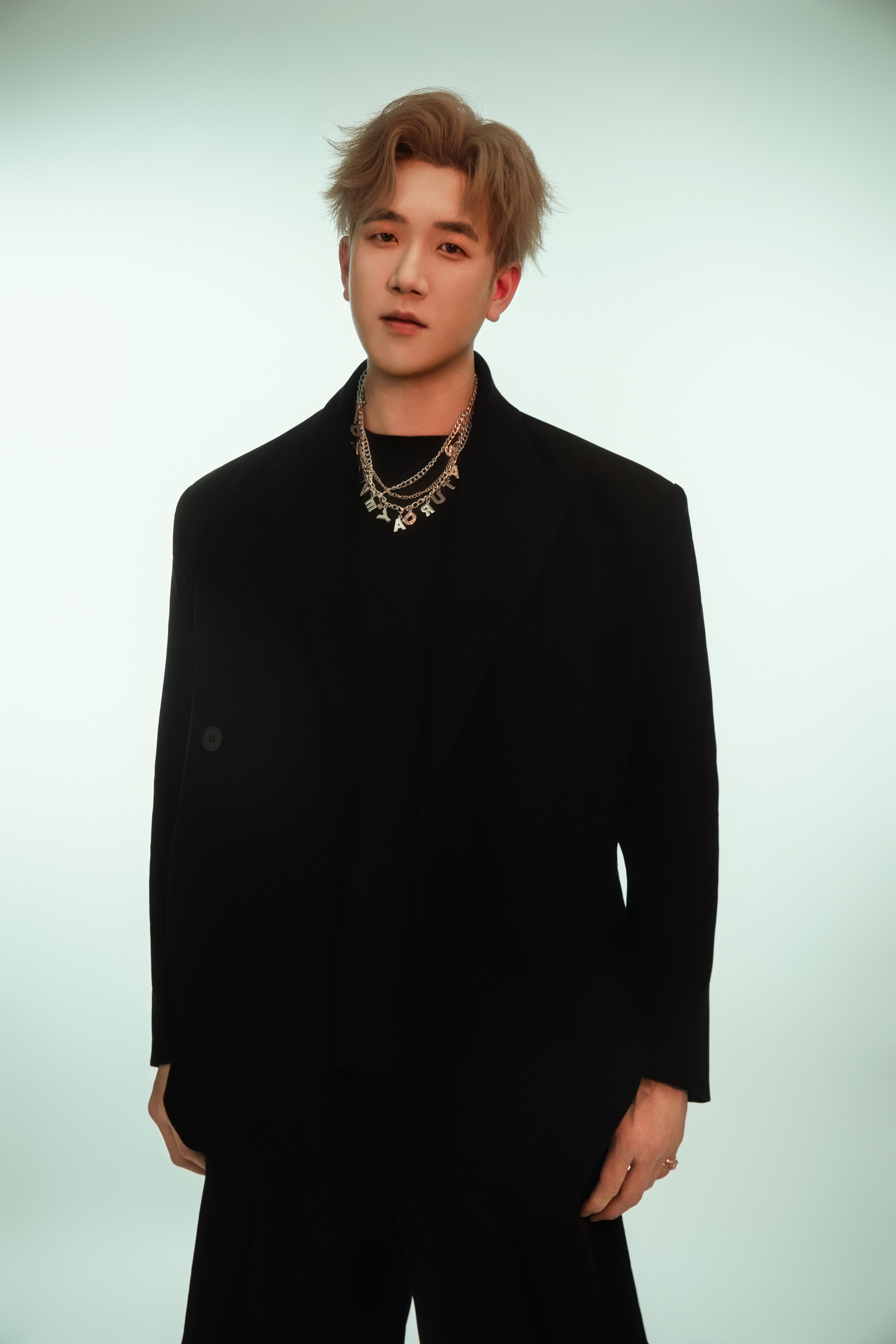 A man poses with a subtle head tilt, emerald hues glowing behind him.