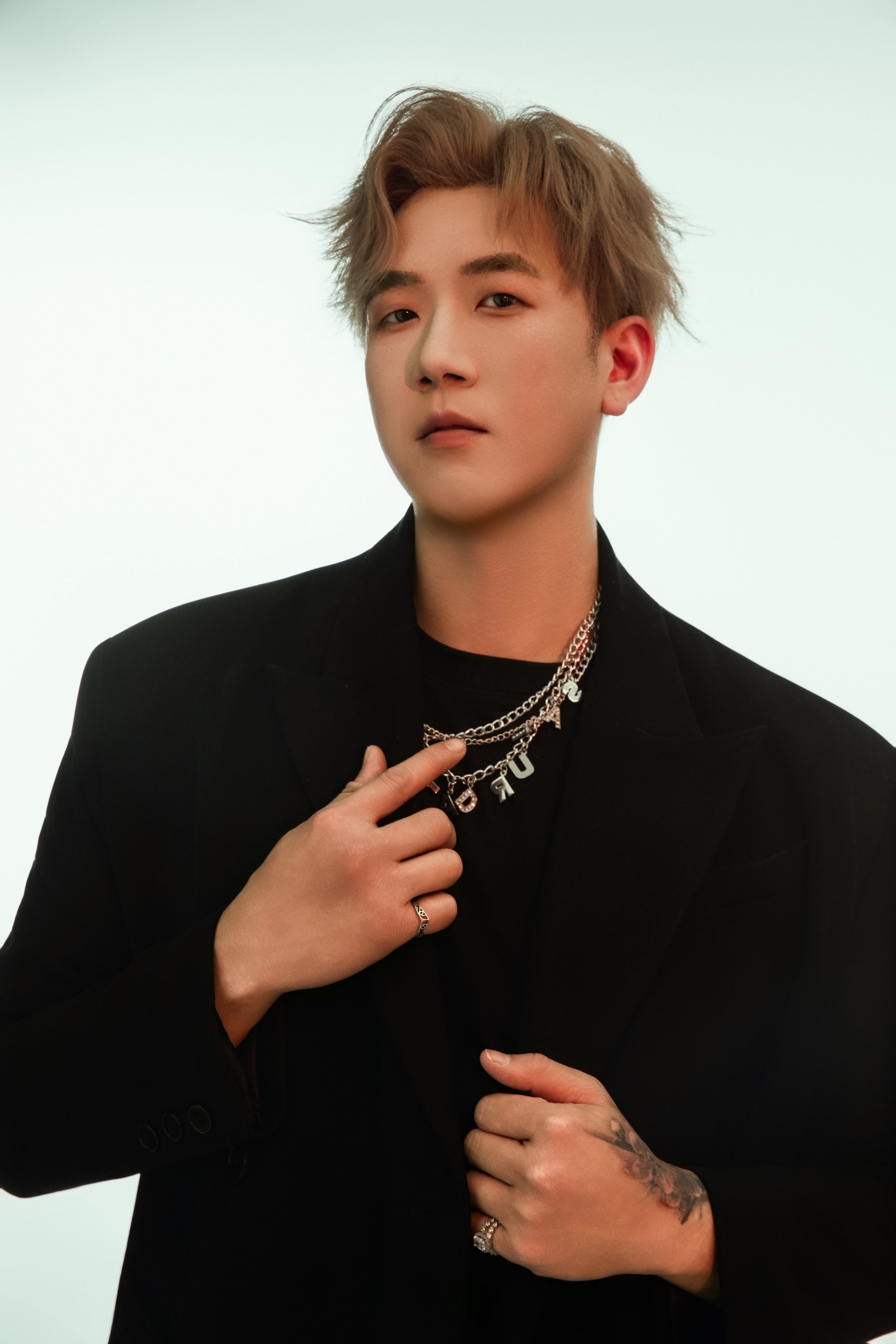 A man stands, adjusting his jacket, with an emerald-tinted background.