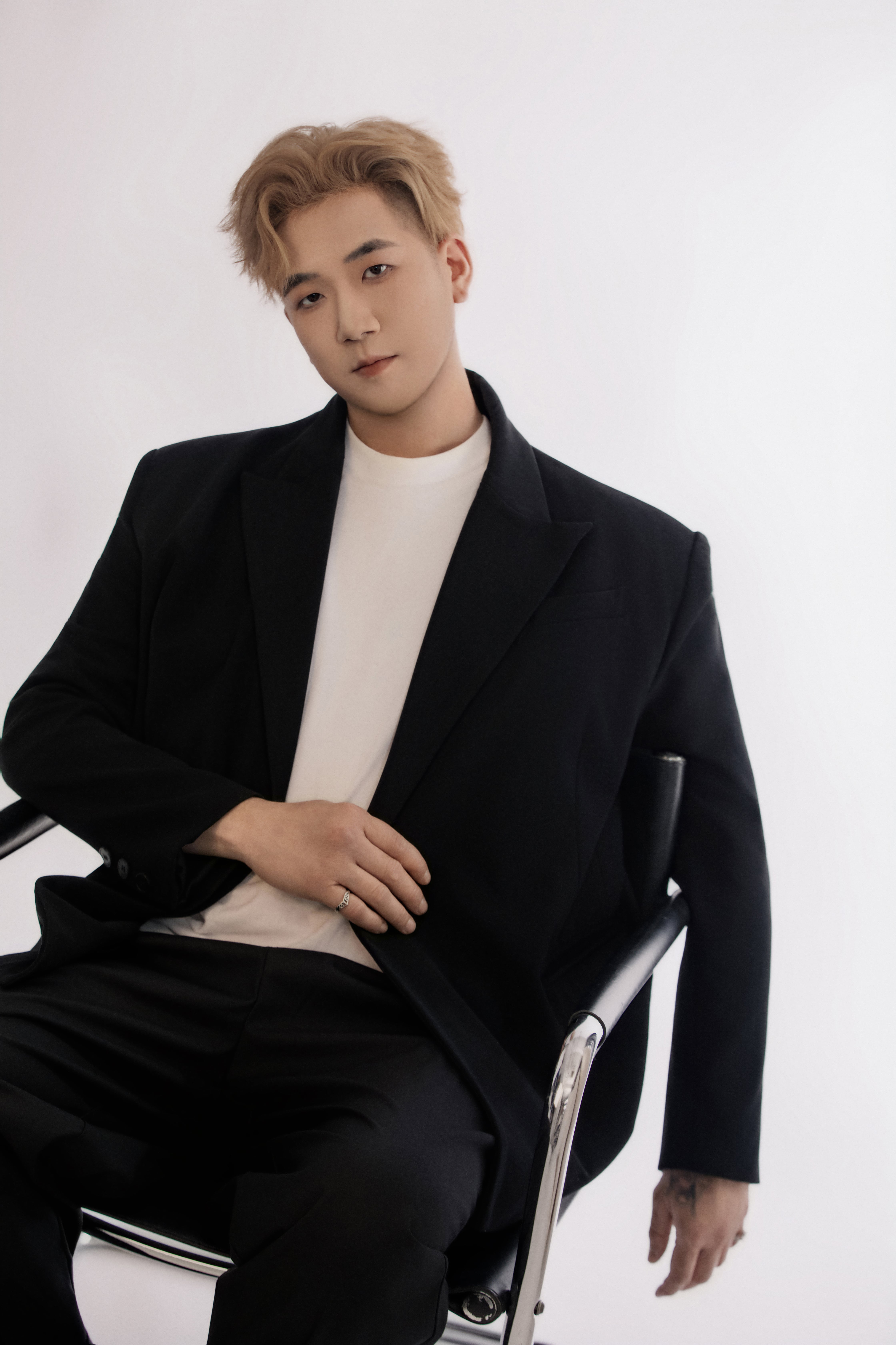 Man seated on a chair, head slightly tilted, looking away in a relaxed pose.