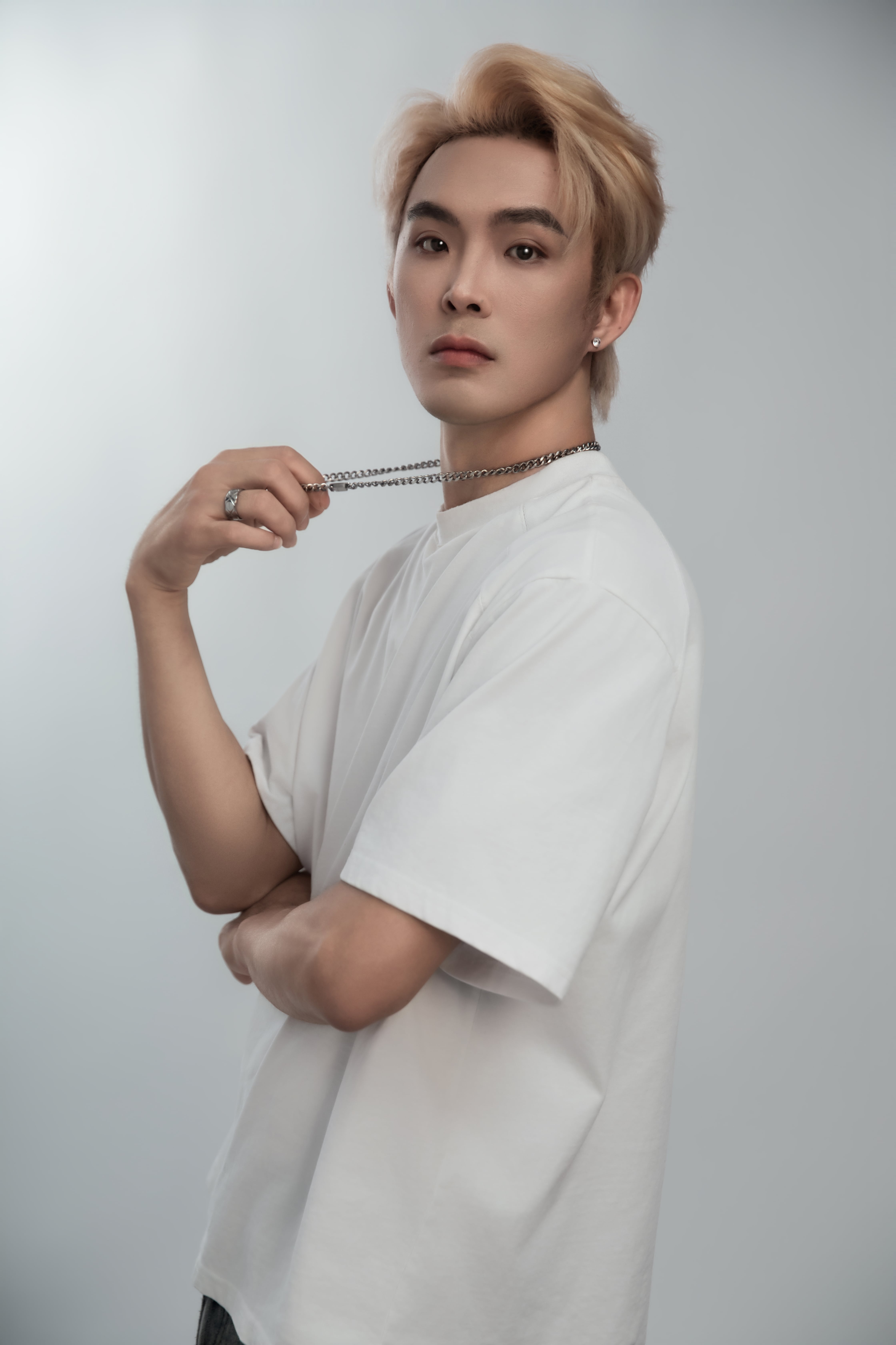 A close-up of a man with his body angled to the side, grabbing his chain and looking at the camera.