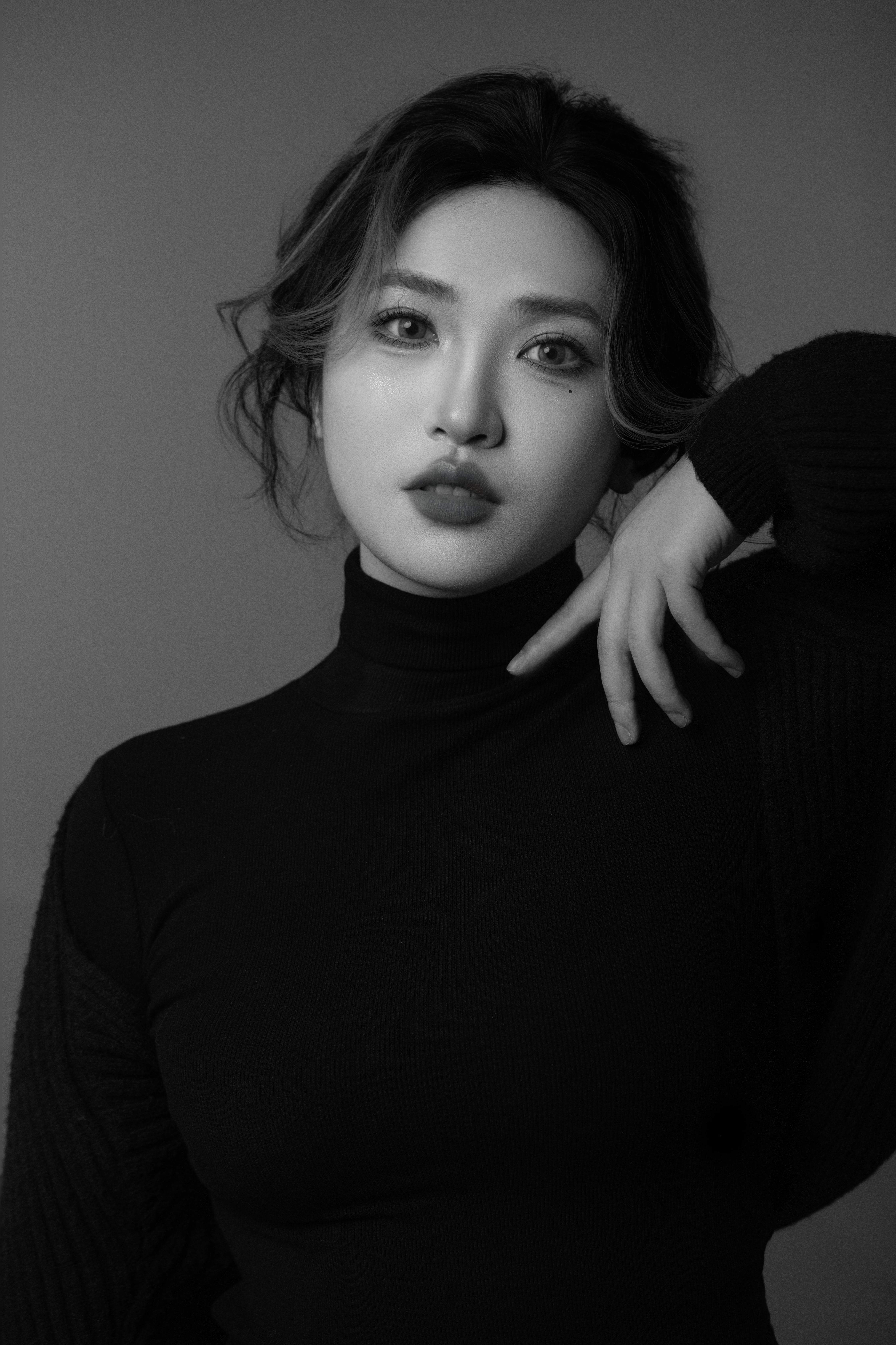 A black-and-white close-up of a woman facing the camera, one hand gently resting on her neck.