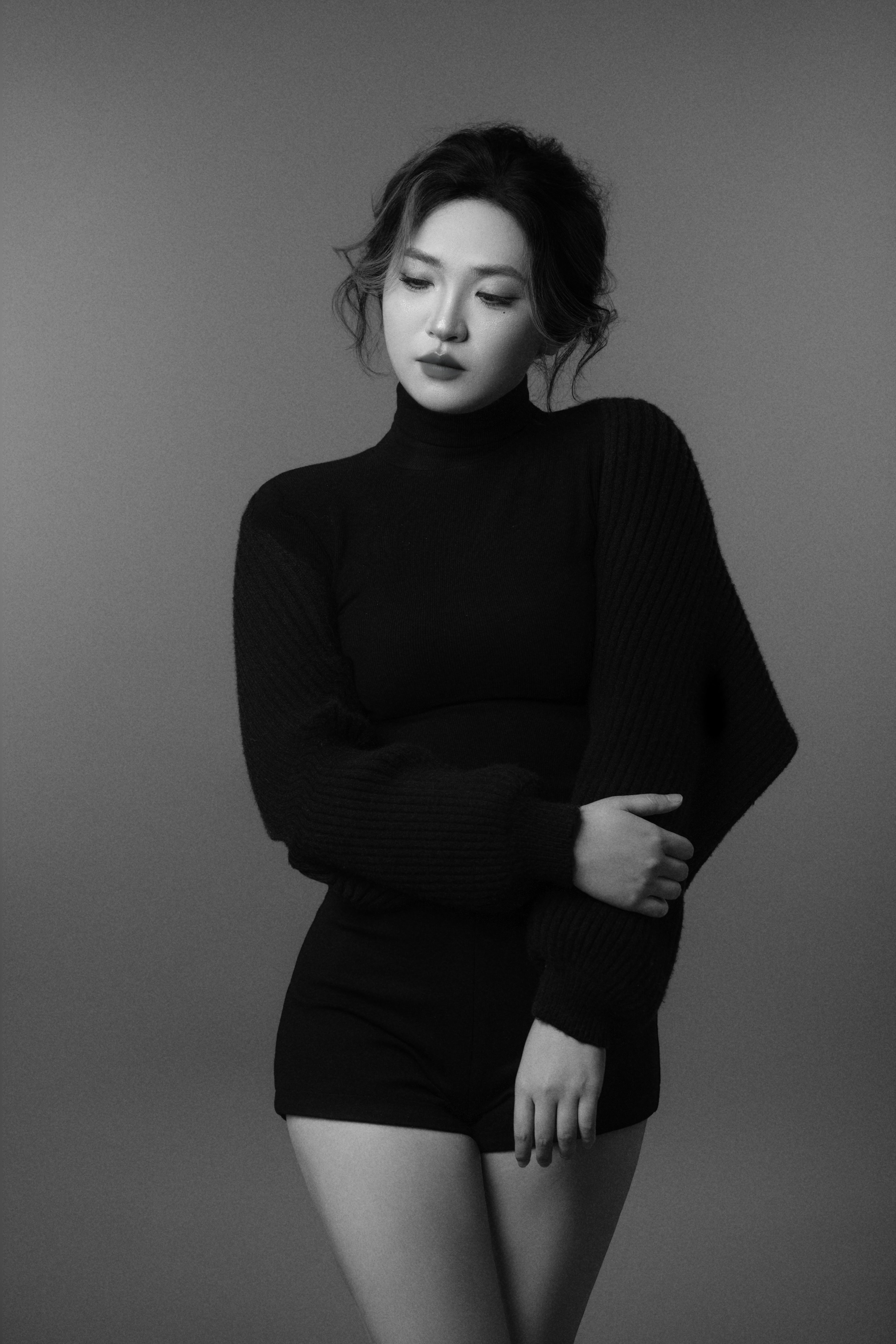 A black-and-white full-body silhouette of a woman posing with both arms down, one arm gently holding the other.