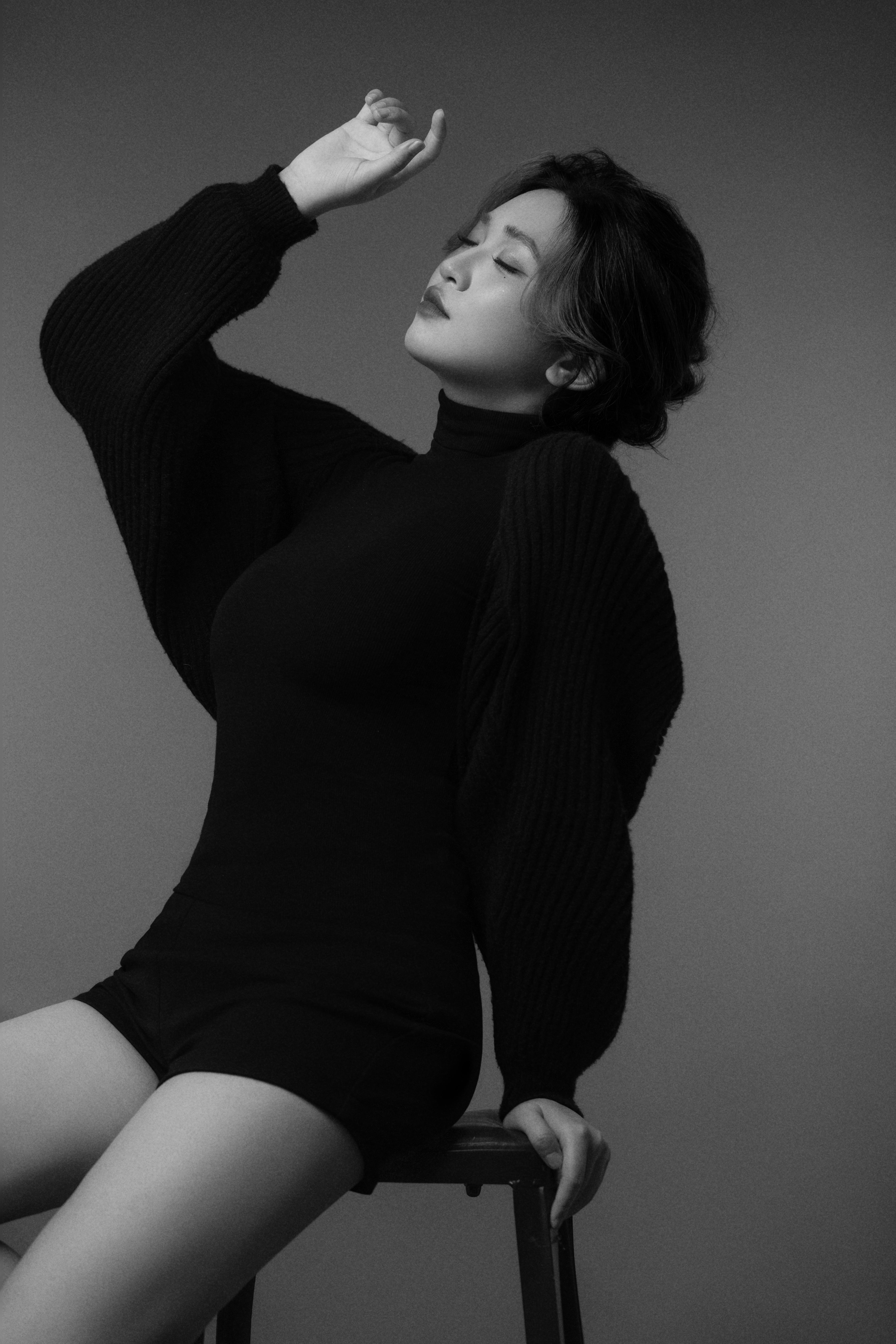 A black-and-white silhouette of a woman leaning back in a chair, her back hand close to her face and eyes gently closed.