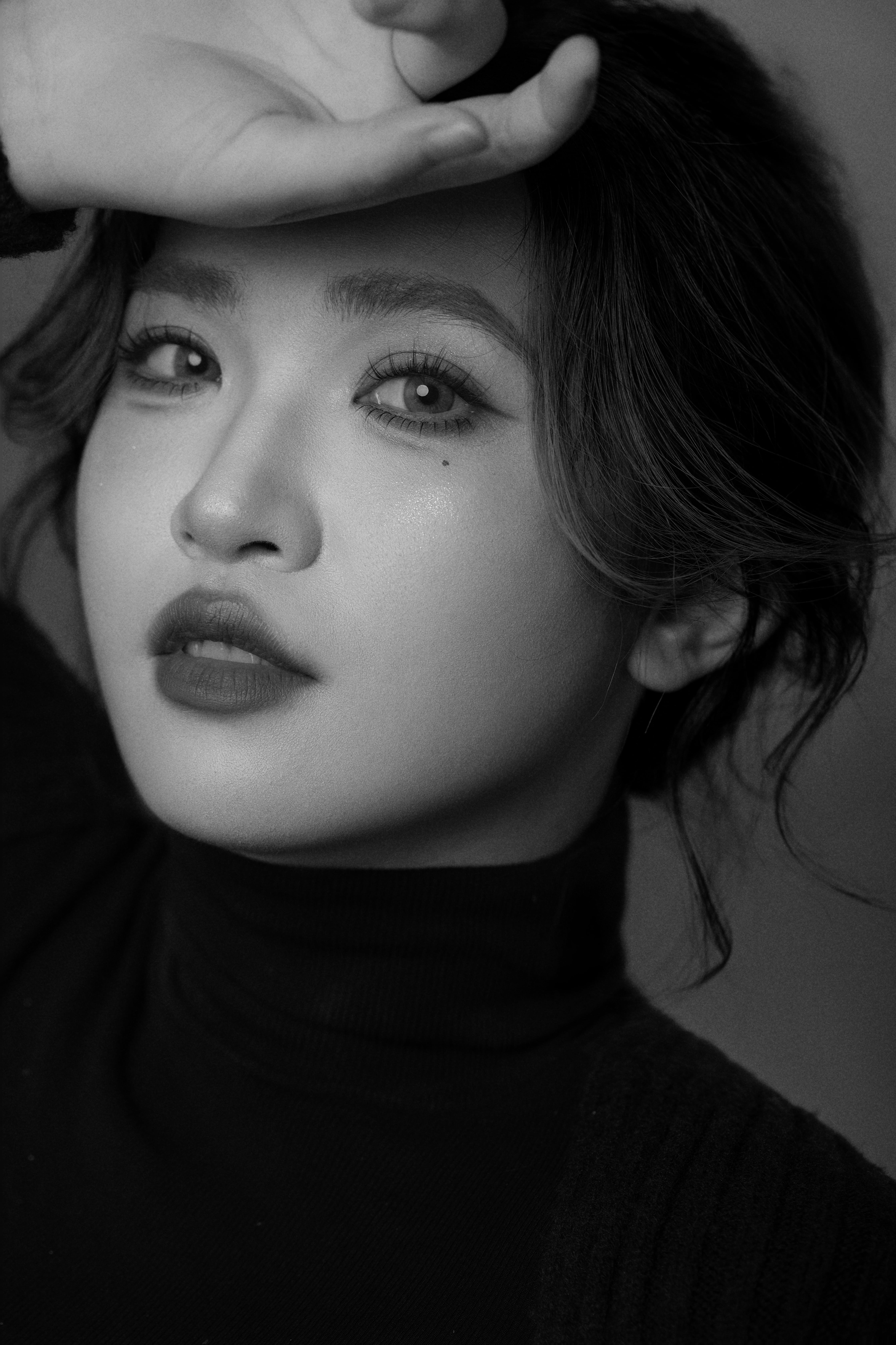 A black-and-white close-up of a woman facing the camera, one hand gently resting on her head.
