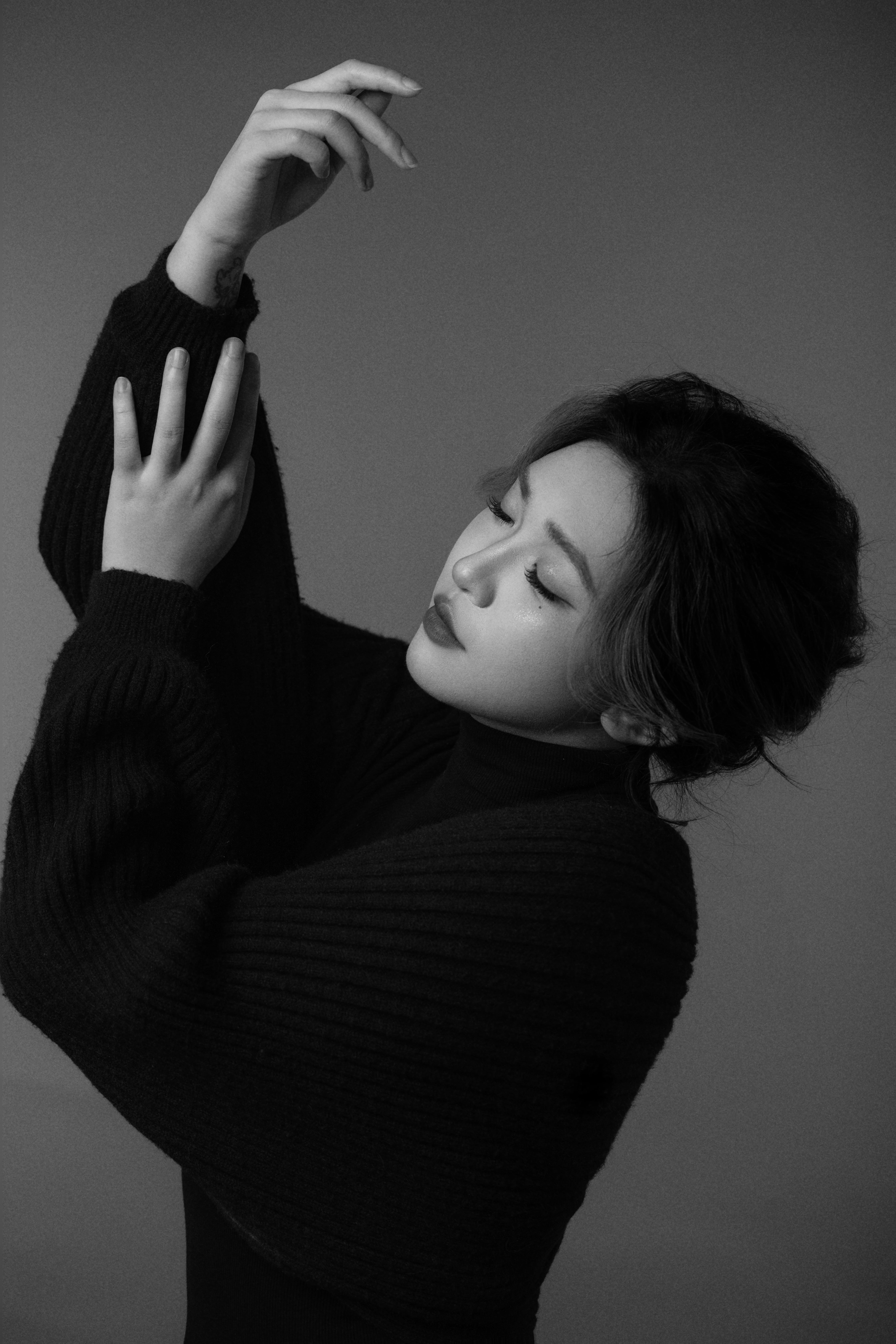 Black-and-white silhouette of a woman with eyes closed, one arm up and the other adjusting her wrist.