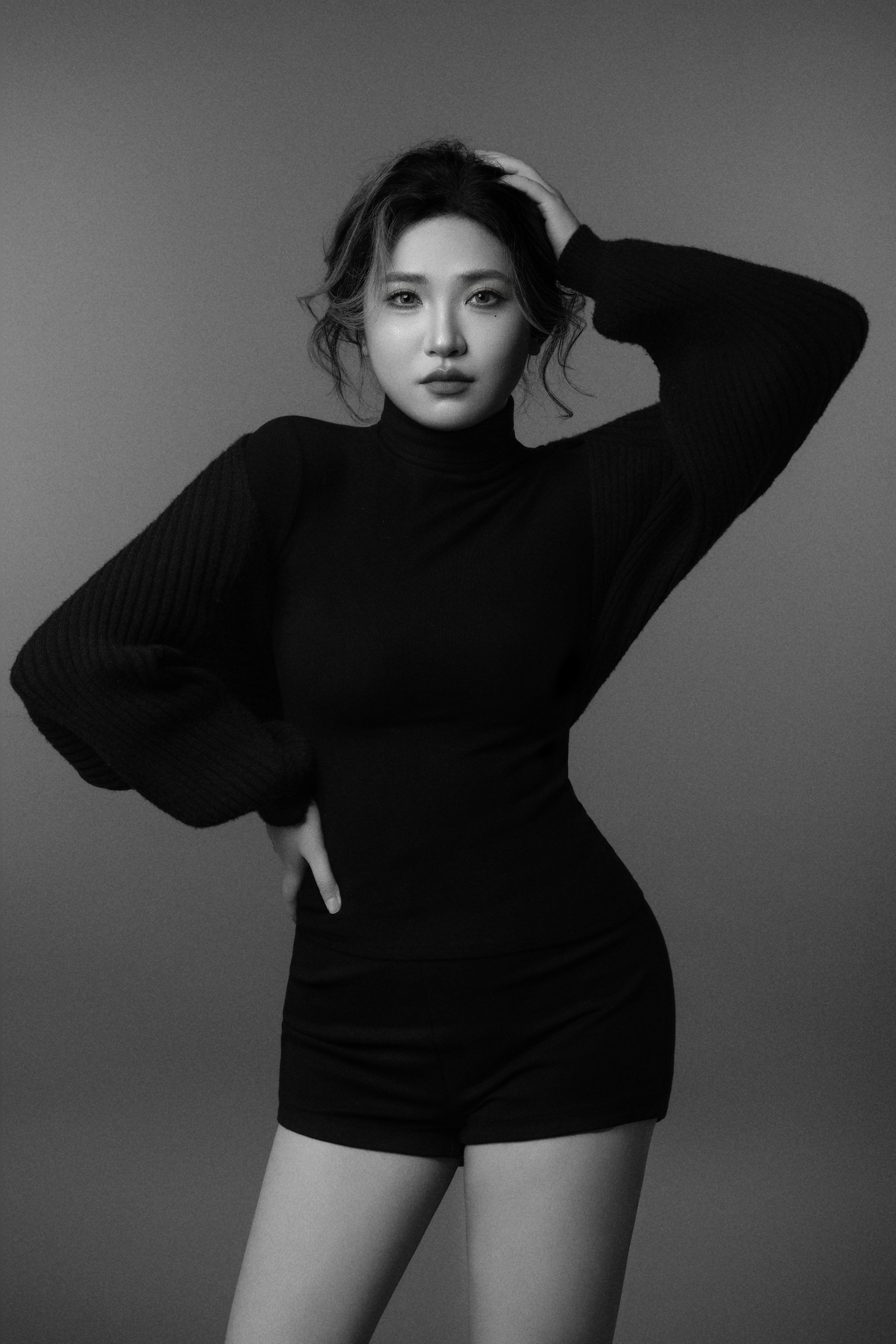 A black-and-white silhouette of a woman facing the camera, one hand resting on her hip and the other on her head.