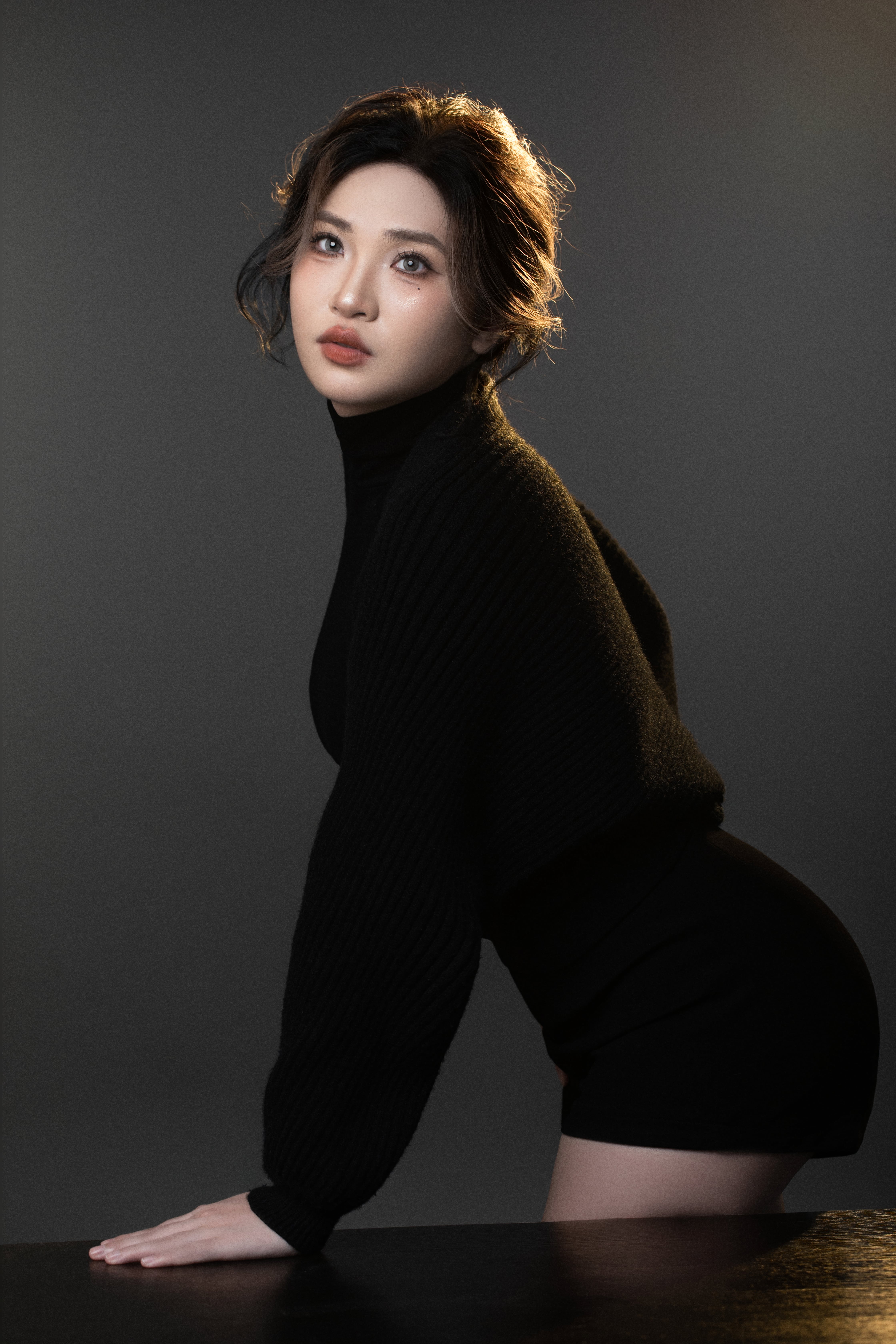 A woman poses from the side with one hand on a table and her hip slightly out.