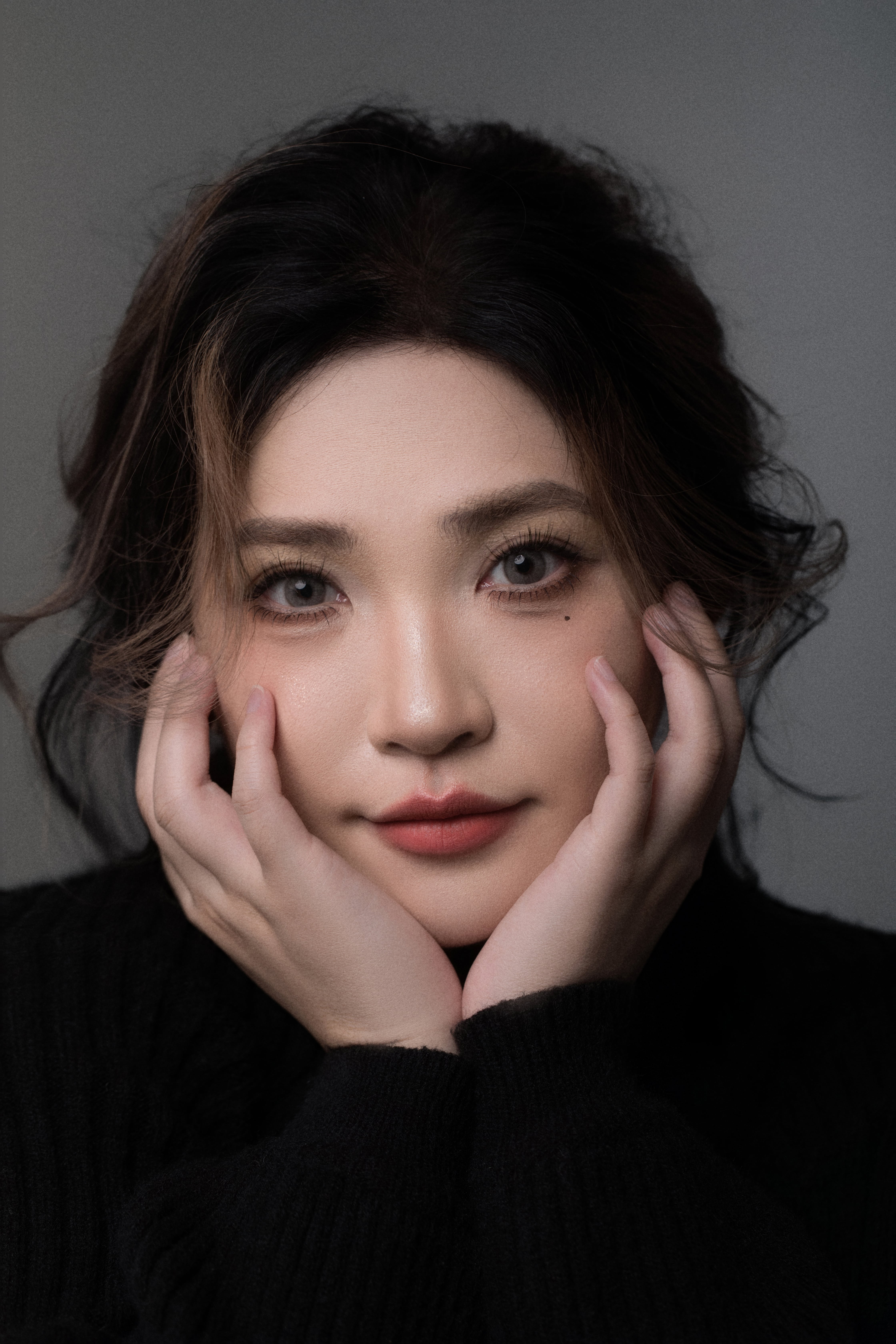 Close-up of a woman looking at the camera, holding her face with both hands