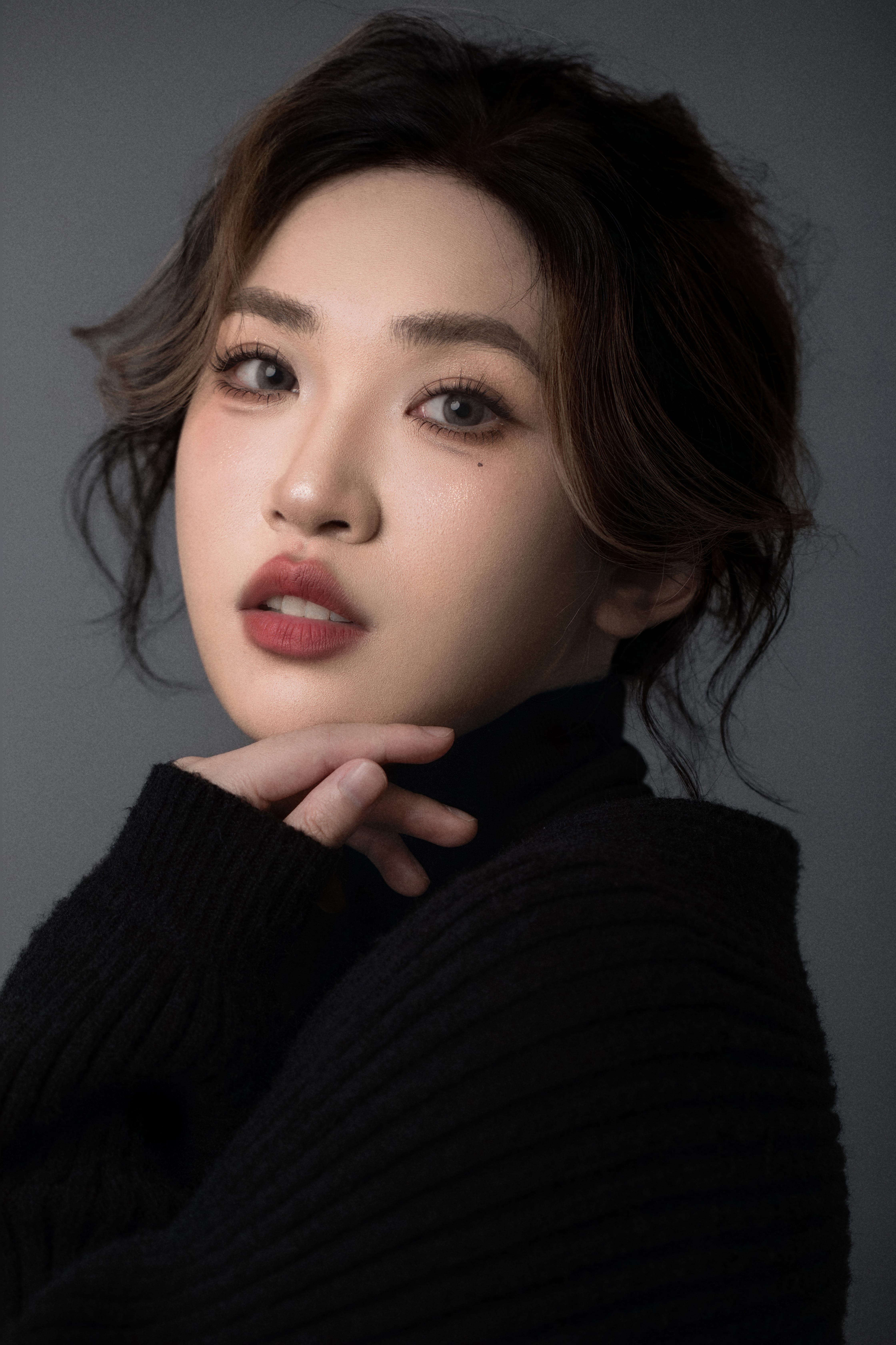 A close-up of a woman facing the camera, with her head gently tilted and resting on her hand