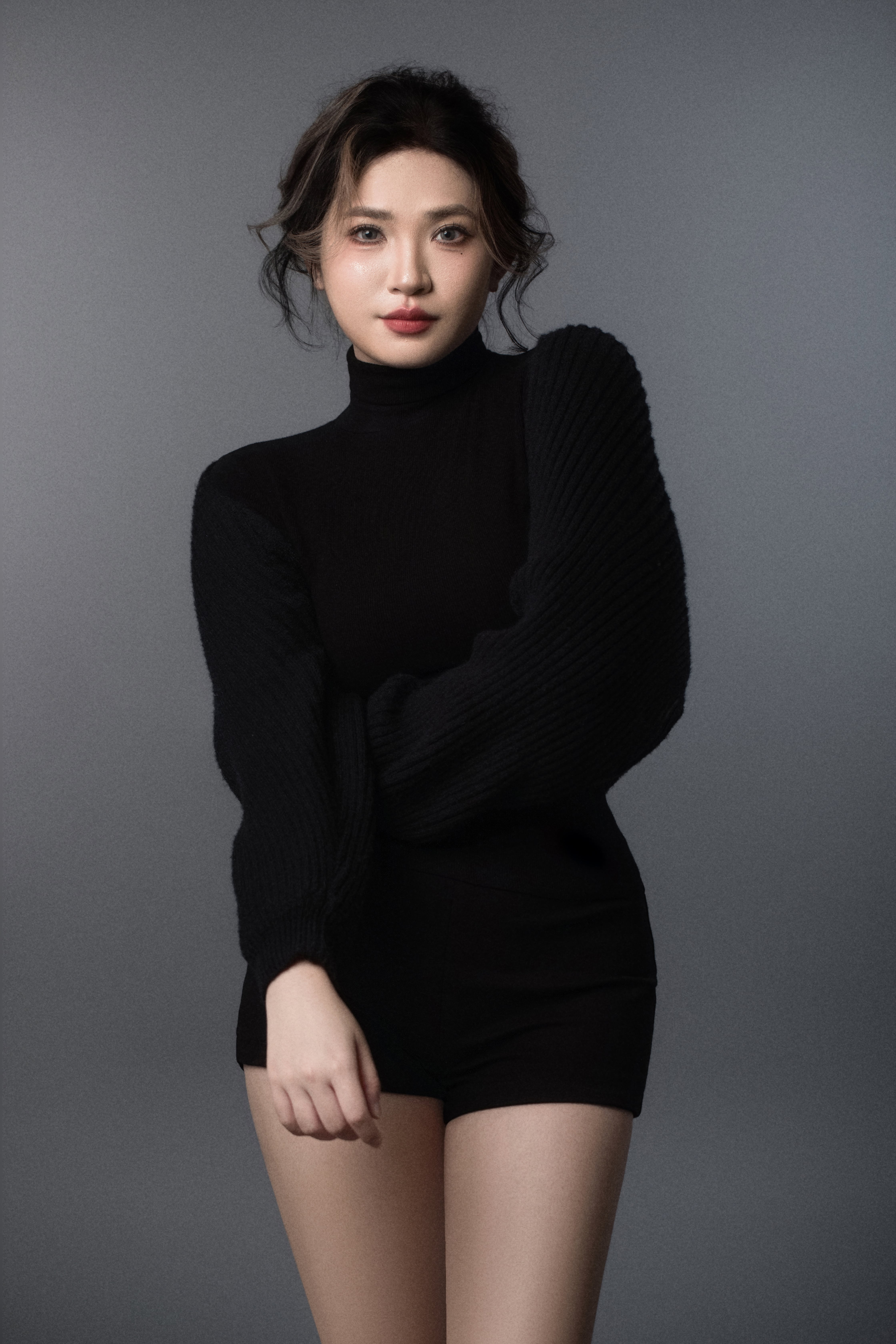 A woman faces the camera, posing with one arm resting beneath the other.