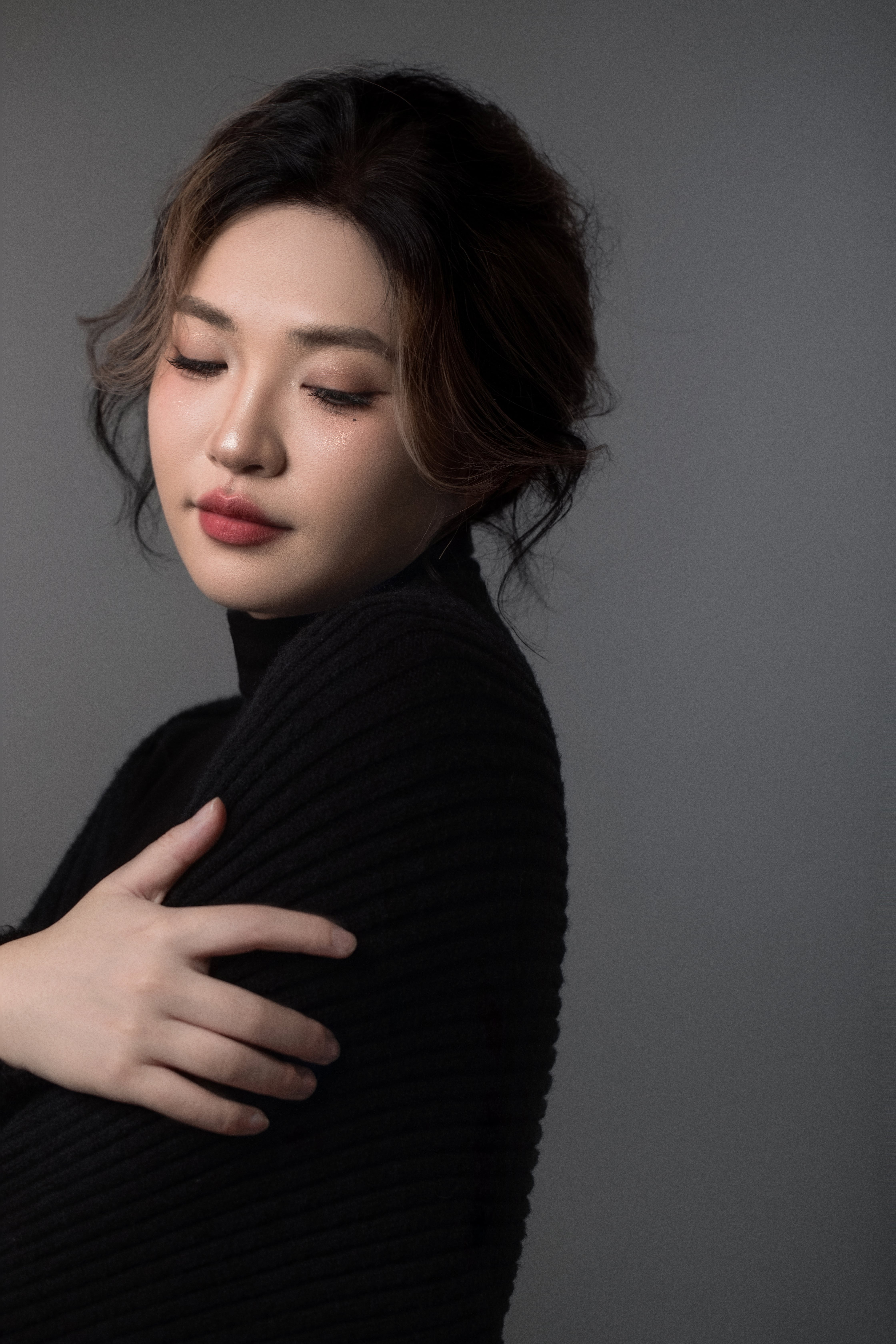 A woman gazes down, embracing herself with her arms crossed in front of her