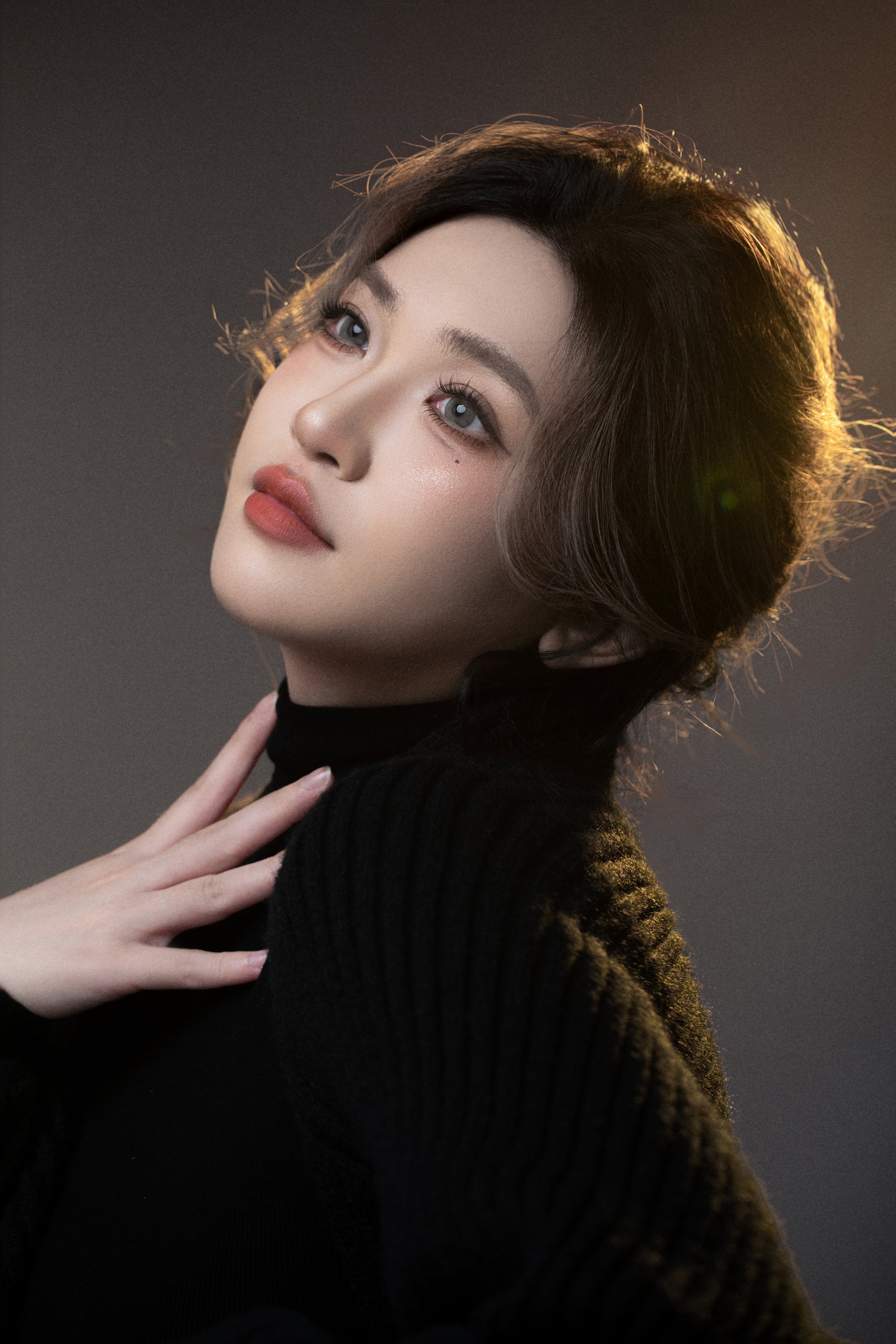 Close-up of a woman looking up, hand on her neck, with golden light on her hair.