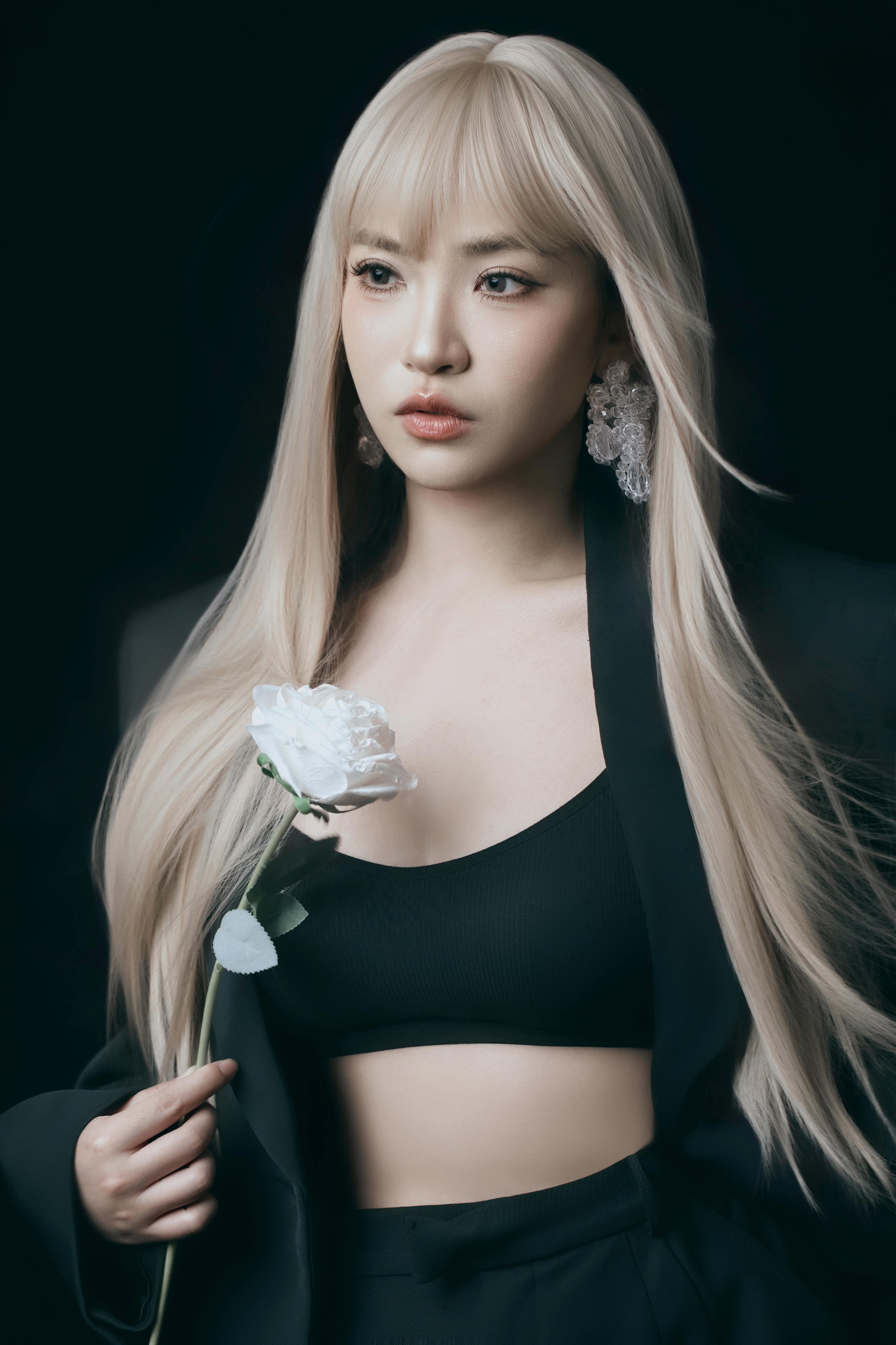 A woman poses holding a flower, gazing away from the camera.