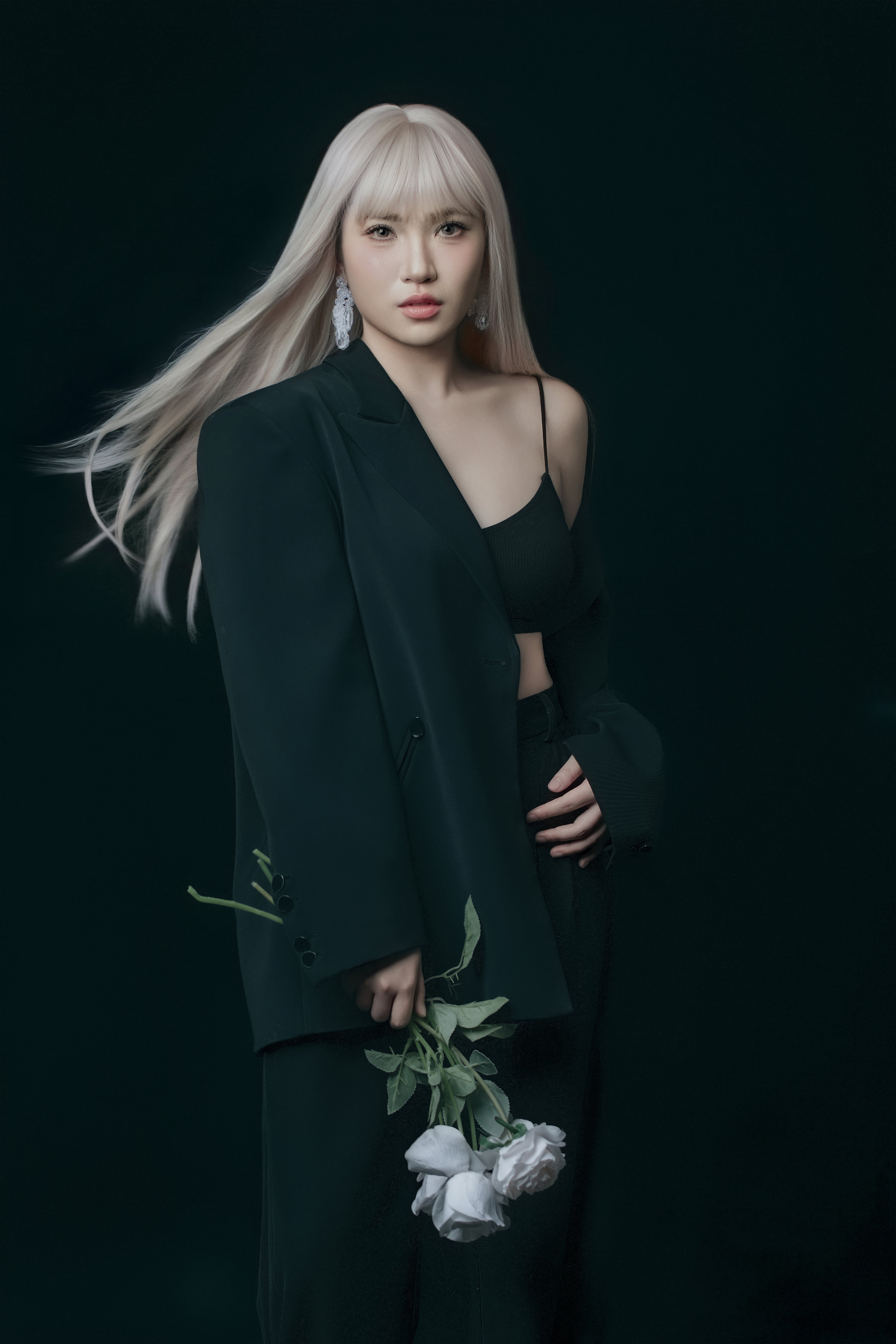 A woman poses in the wind, hand on waist, holding a flower with the other hand.