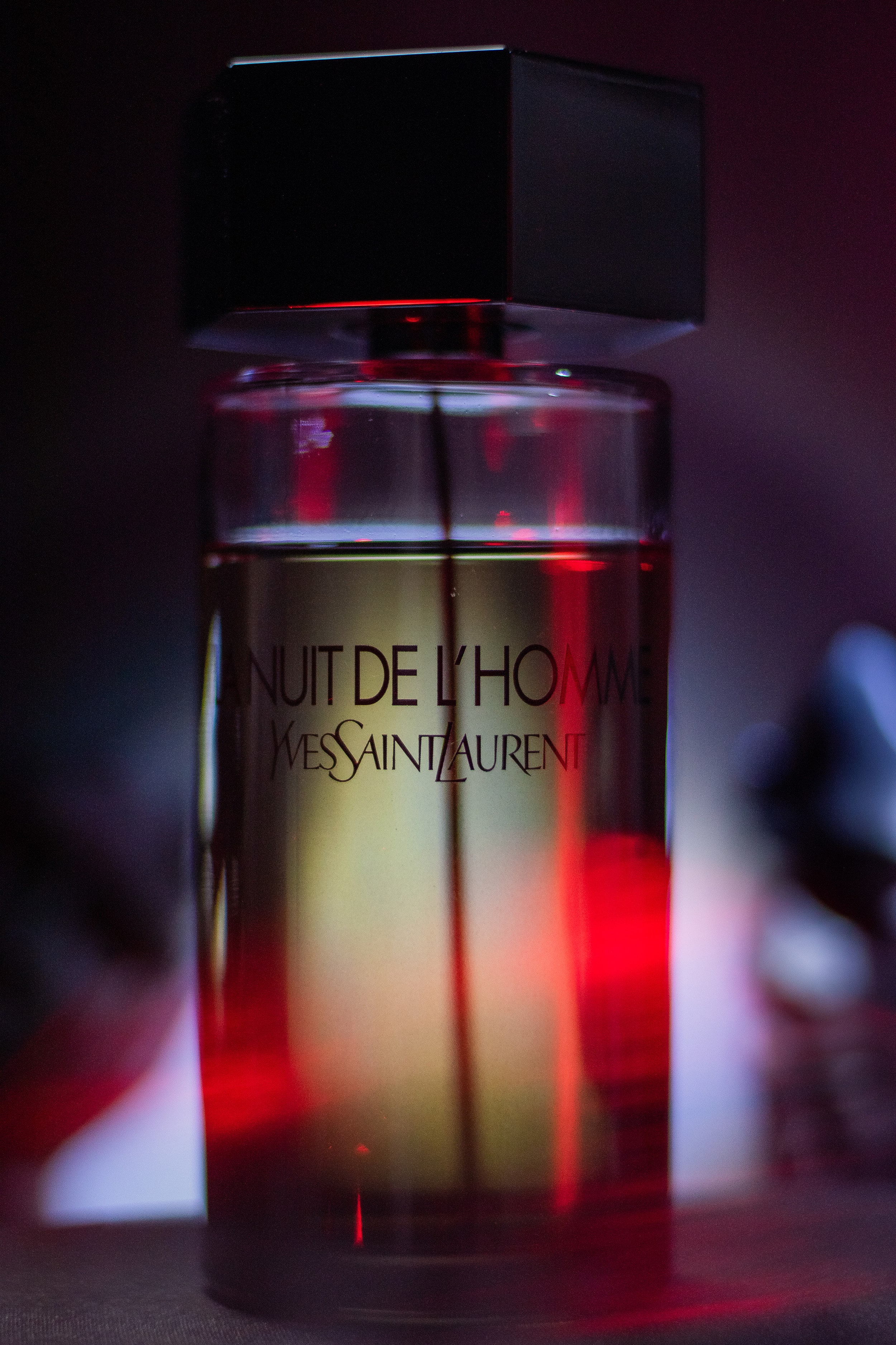Angled view of La Nuit de L’Homme bottle with vibrant red lighting in the background for a dramatic, film-inspired look.