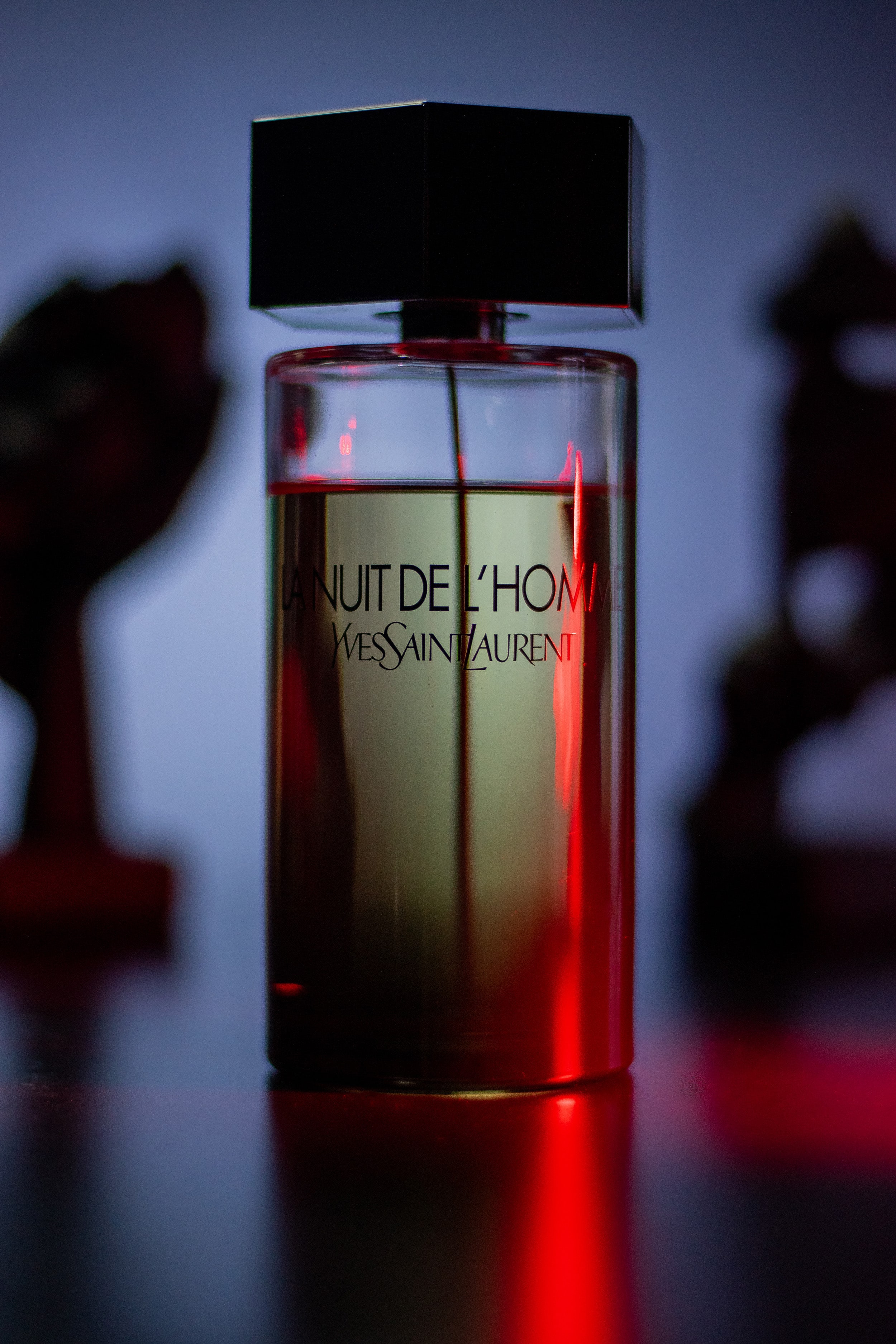 La Nuit de L’Homme bottle photographed with a subtle red light casting dramatic shadows.