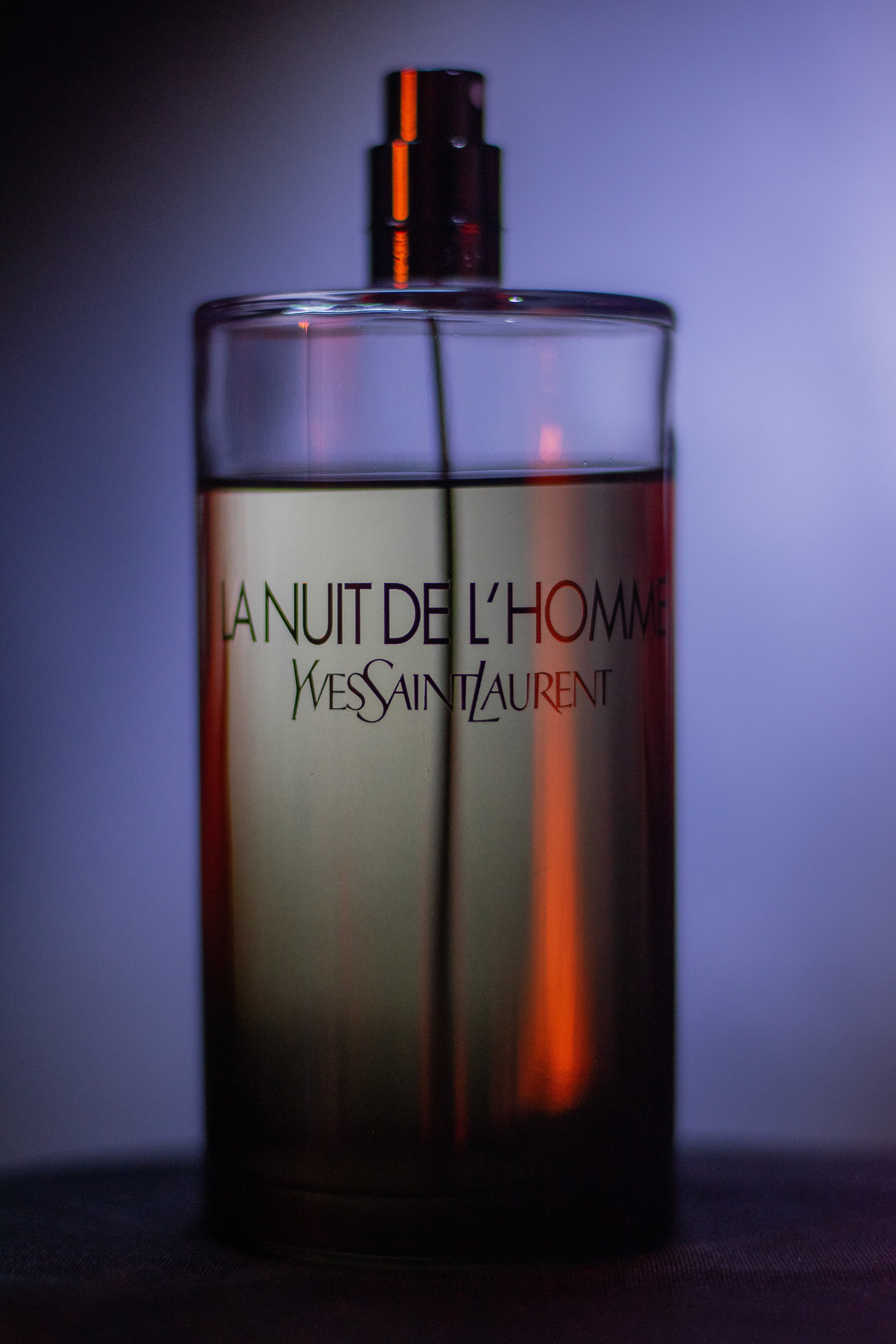 La Nuit de L’Homme Cologne in a high-contrast film-style setup with white background lighting.