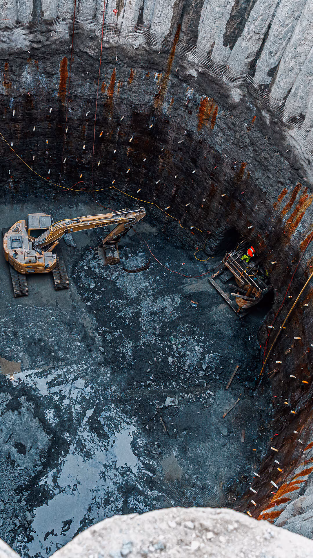 Excavator working at the bottom of a deep circular construction pit with muddy ground.