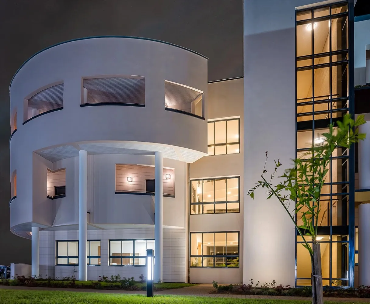 Modern white building with curved walls and large windows illuminated at night.