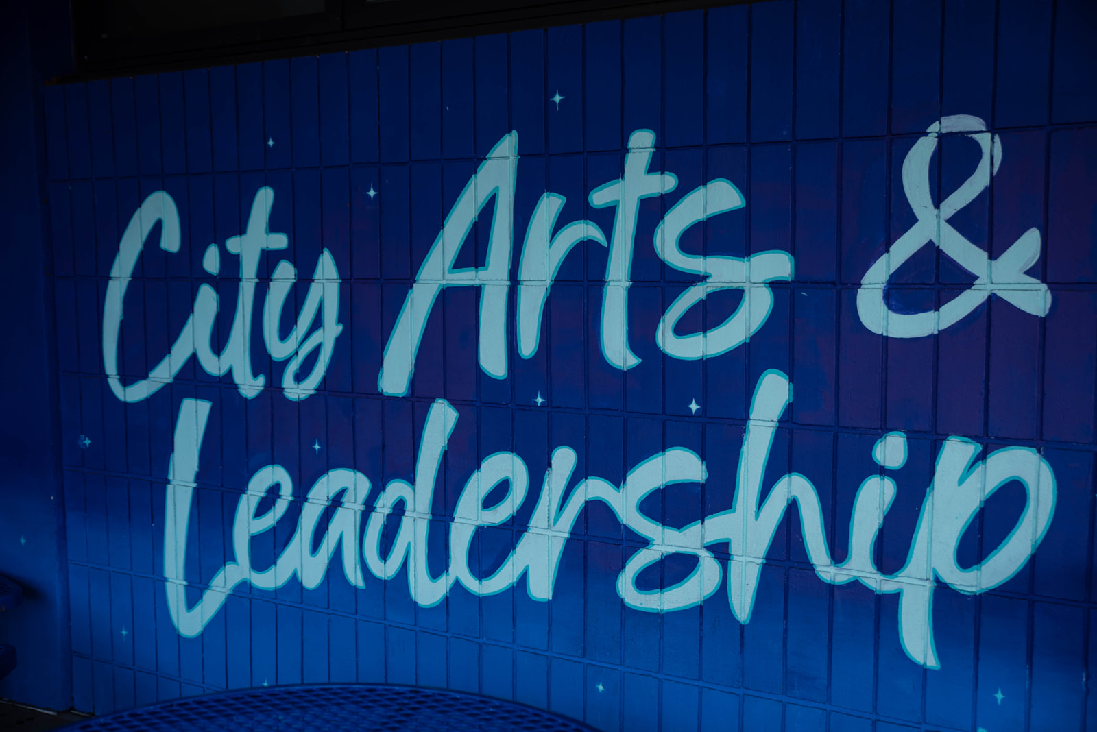 Blue wall mural with white cursive text reading 'City Arts & Leadership' and small star-like decorations.