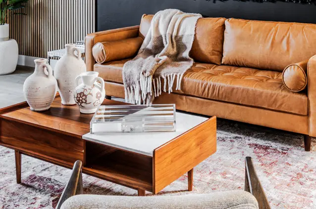 Tan leather sofa with a cozy throw blanket next to a wooden coffee table holding decorative vases in a stylish living room.