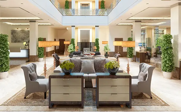 Spacious, modern hotel lobby with neutral-toned seating, decorative plants, floor lamps, and a high ceiling with balcony.