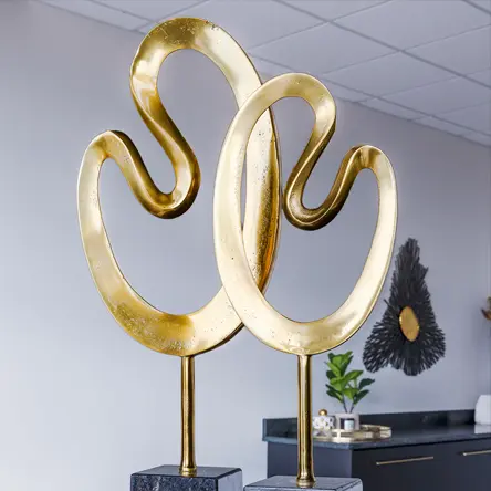Modern gold abstract sculptures on black marble bases in a contemporary interior setting.