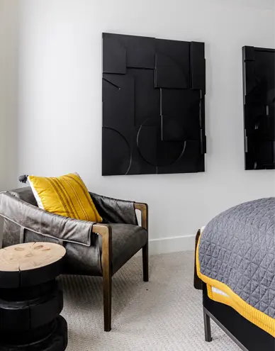 Modern bedroom corner with a gray leather chair featuring yellow cushion, black abstract wall art, and a gray bedspread with yellow trim.