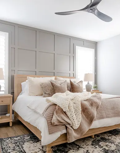 Cozy bedroom with wooden bed frame, layered beige and white bedding, textured throw blanket, and modern ceiling fan.