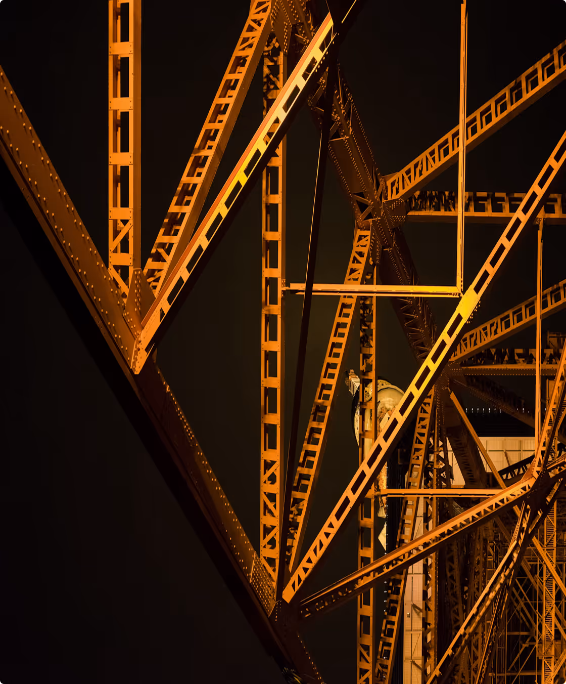 Close-up of orange steel bridge trusses and beams illuminated at night.