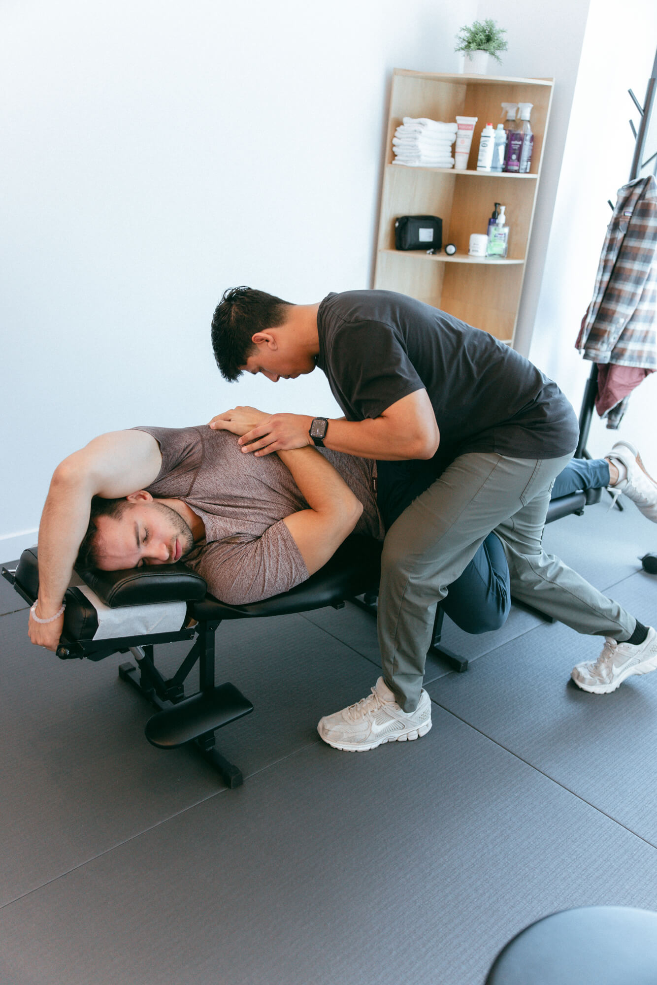 A man lying on a black therapy table receiving a physical therapy adjustment from a therapist in a modern clinic room.