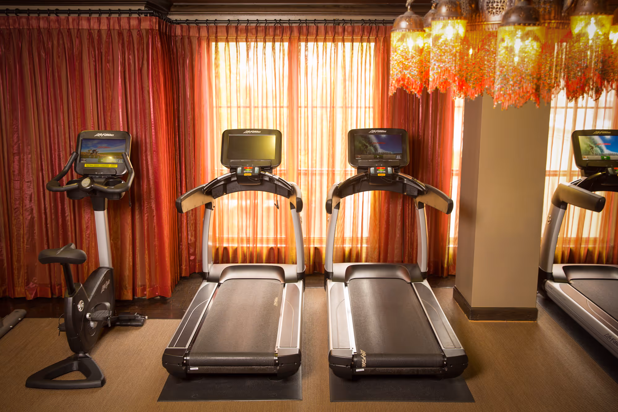 Luxury gym with modern treadmills and exercise bike, featuring red drapery in Dallas, TX.