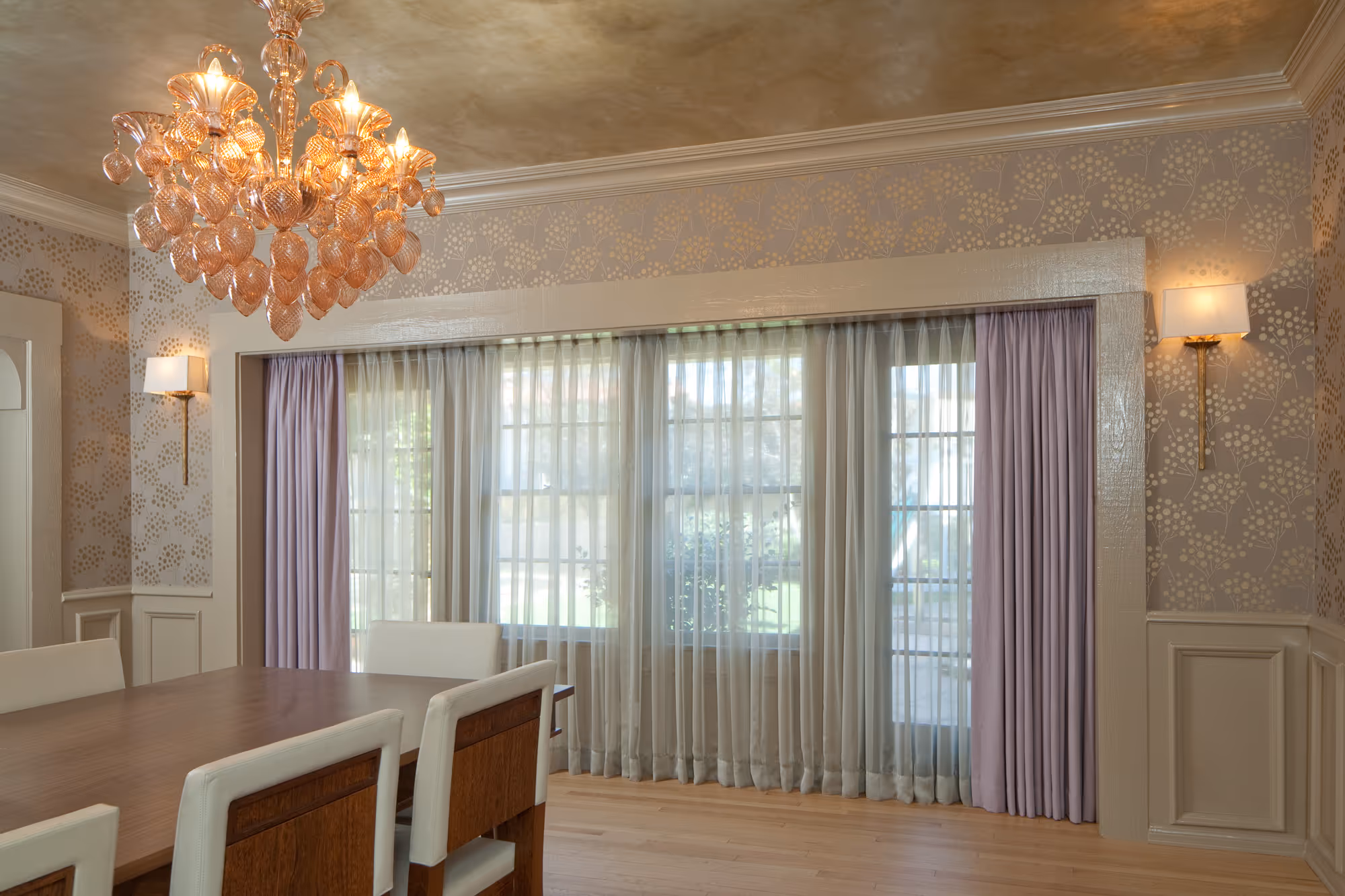 Elegant Hollywood dining room featuring sheer and purple drapes, a modern chandelier, and a stylish wooden dining table.