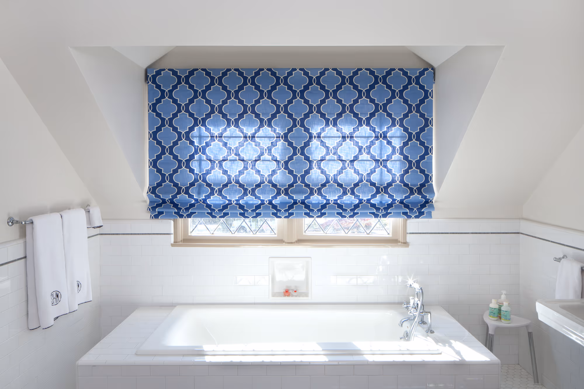 Elegant bathroom in hollywood ca featuring a blue patterned roman shade over a modern tub with white tiles.
