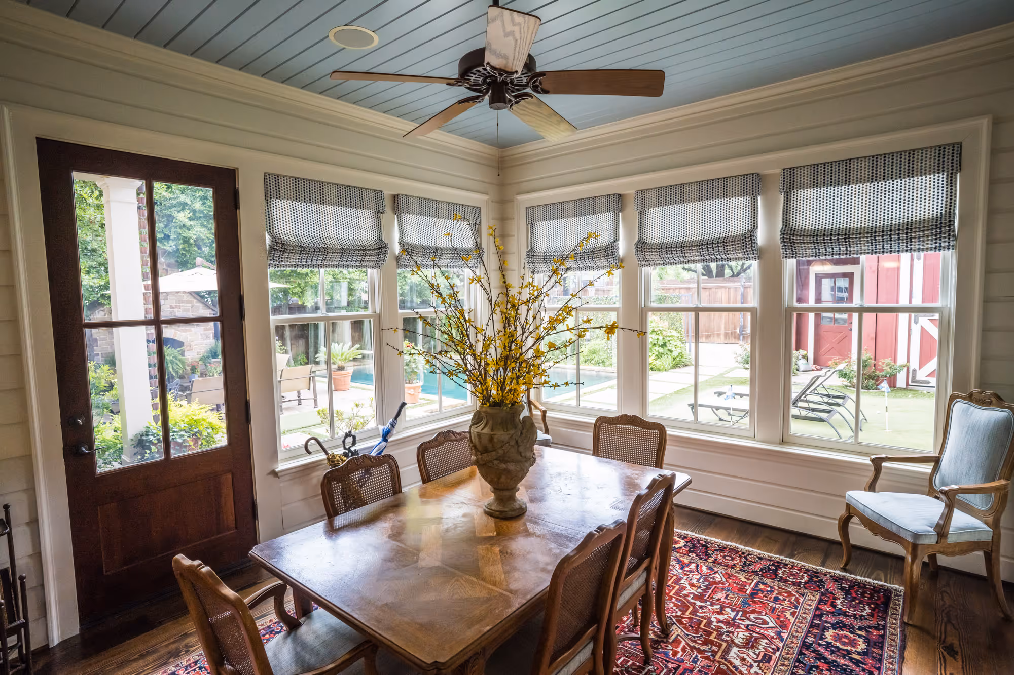 Cozy dining room with polka dot roman shades and a wooden table, featuring yellow flowers and a view of the outdoor garden in Dallas, TX.